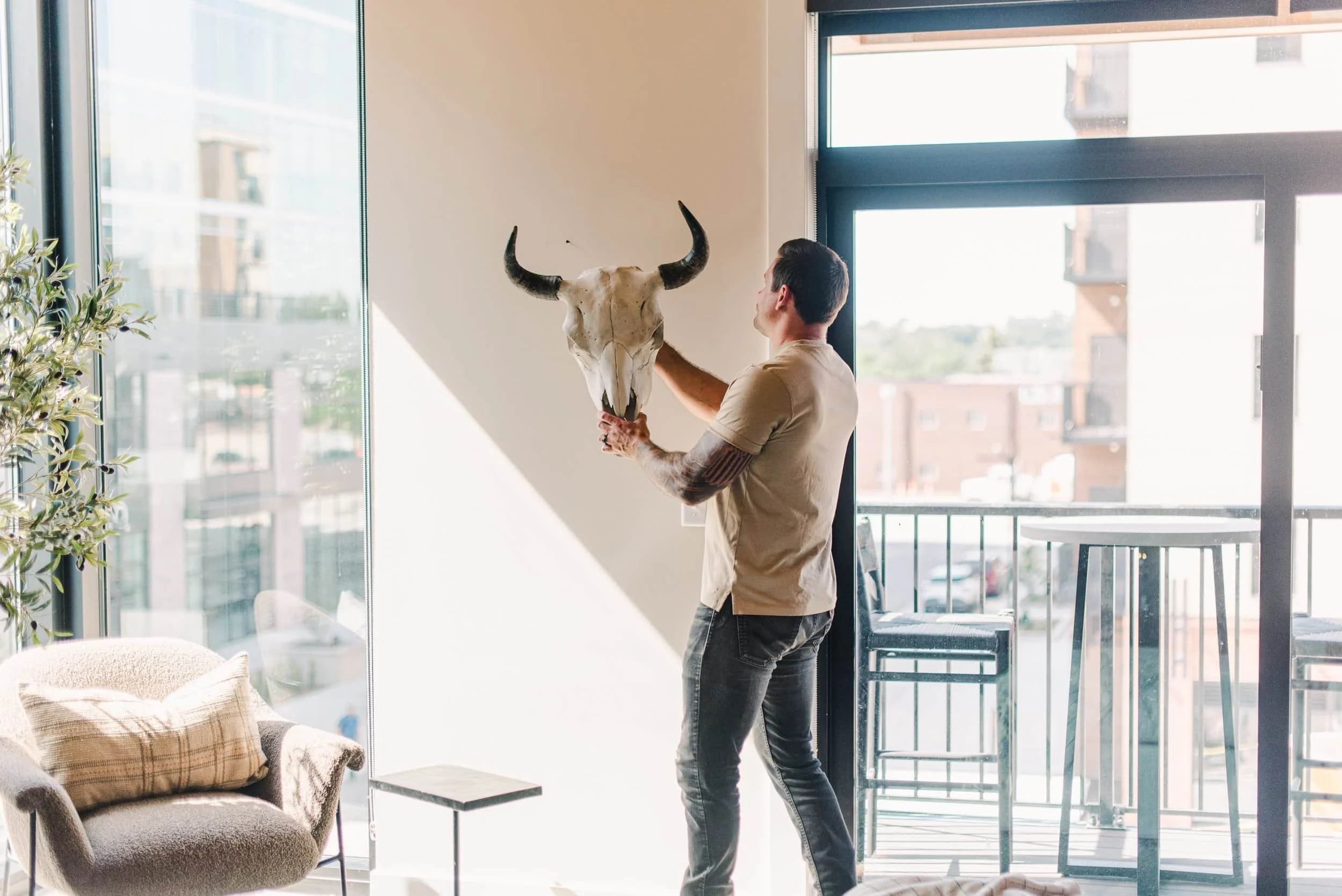 Cole DeBoer holding a bull skull is preparing to mount it on a white wall in a bright apartment