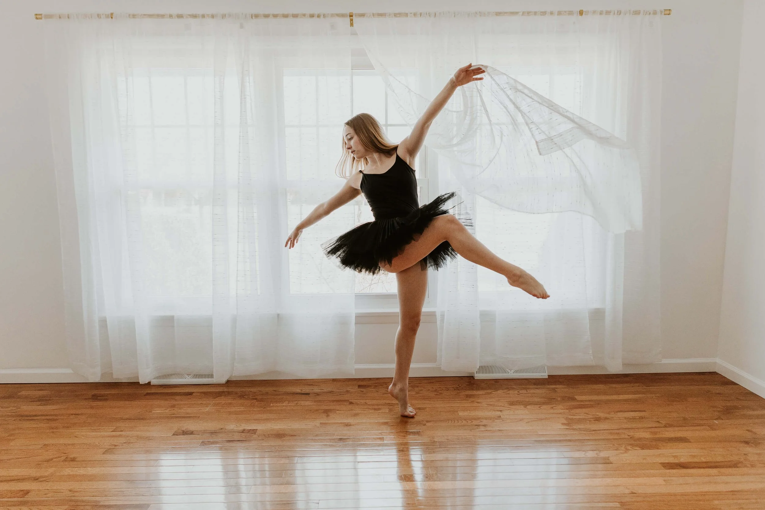 Playfully dancing with the curtains, a ballerina strikes a pose.