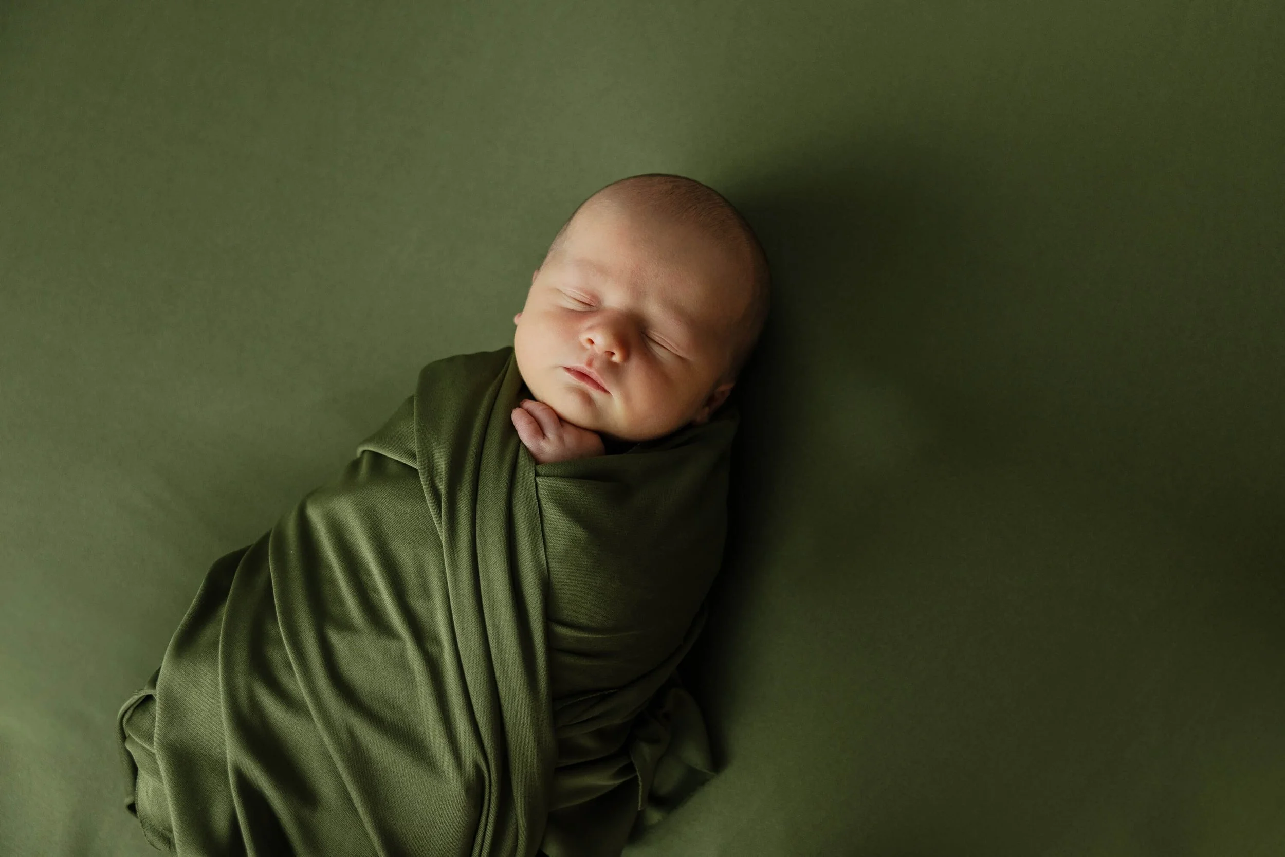 Baby Henry sleeps while swaddled in a green blanket against a matching green backdrop