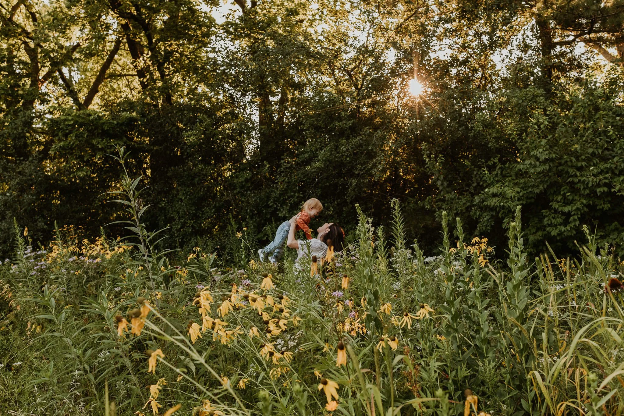 A glimpse of a mother tossing her toddler into the air just beyond a patch of wild flowers in Bloomington IL