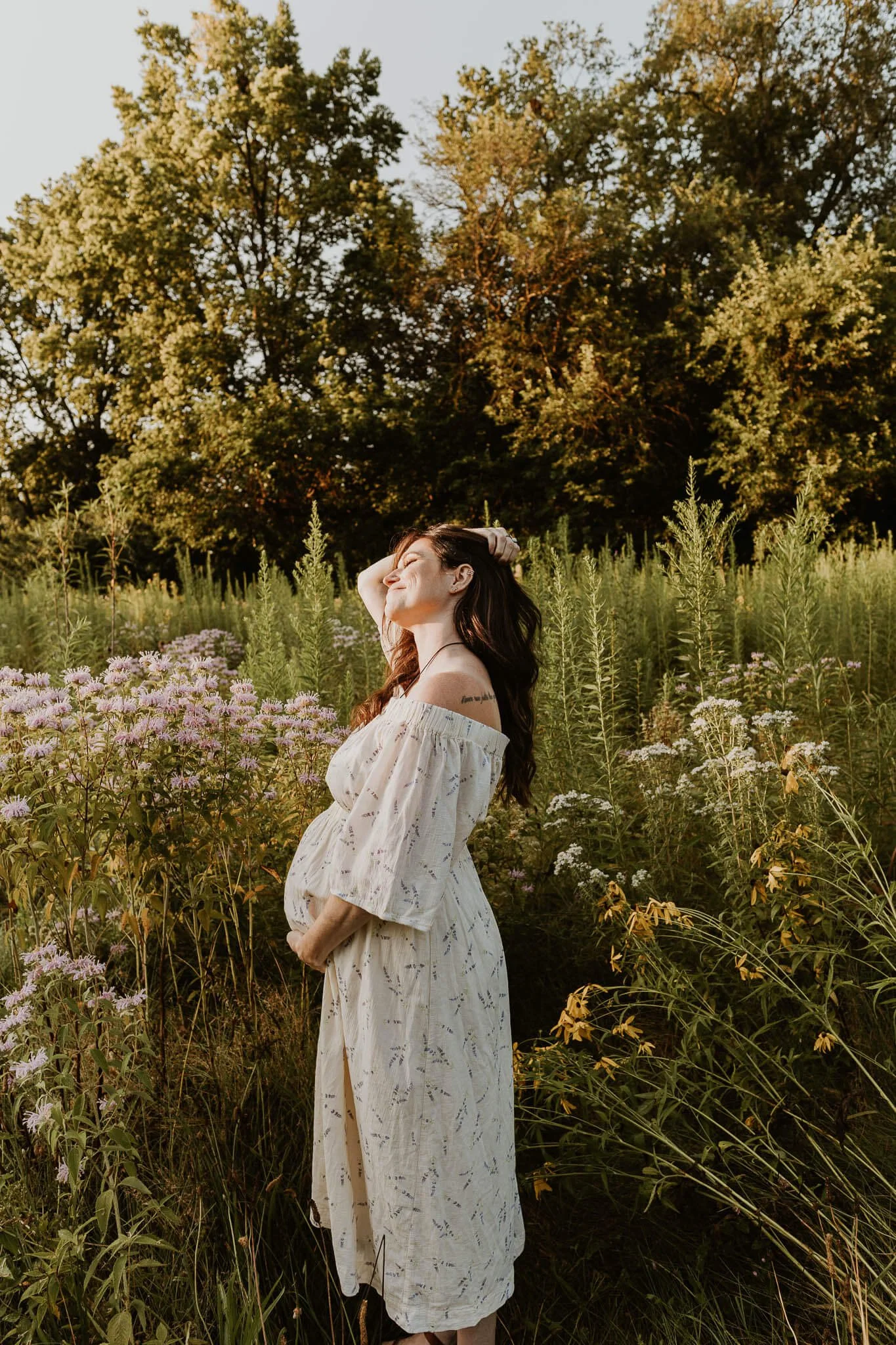 A mother smiles serenly in a wildflower field at Underwood Park, holding her round pregnant belly
