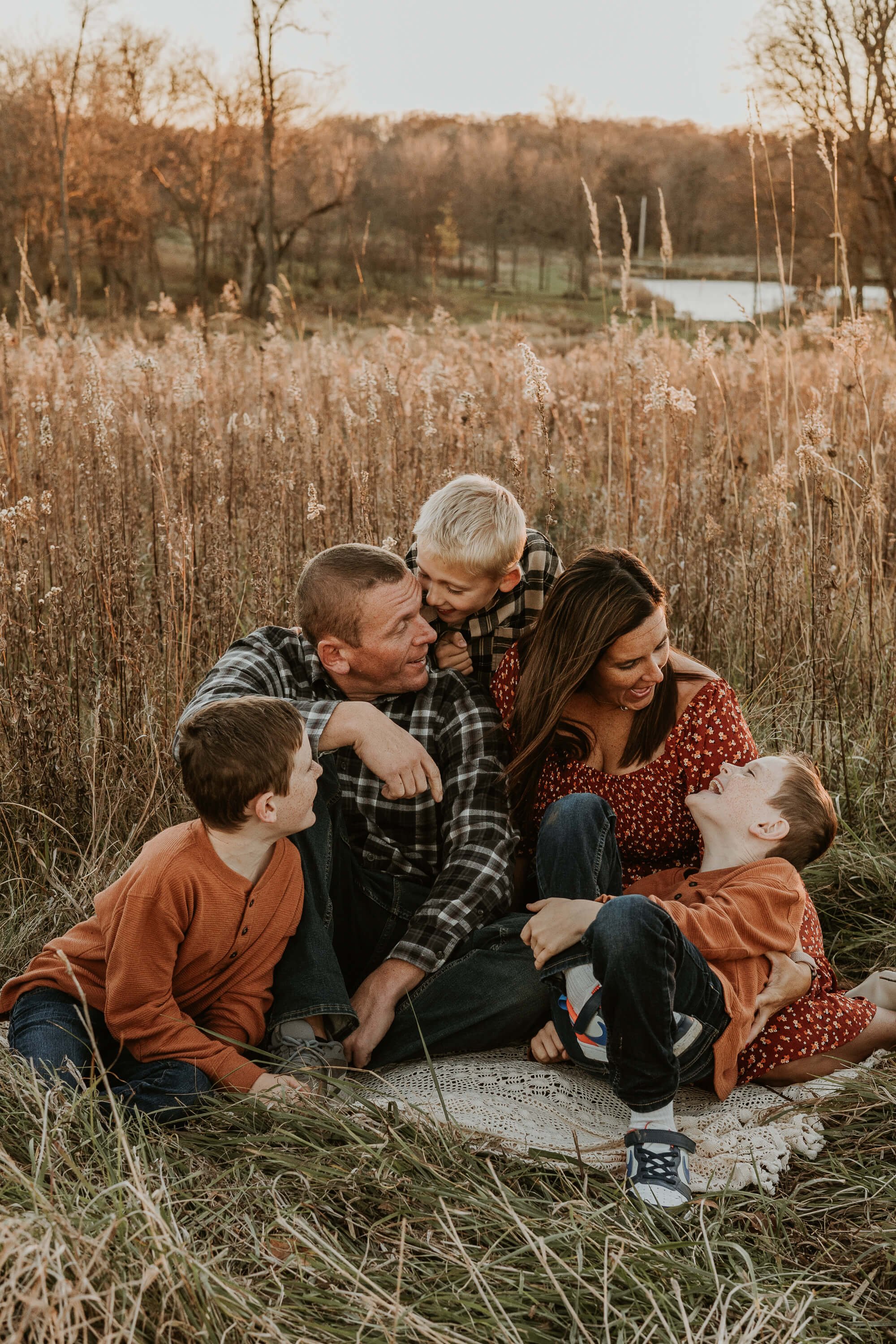 A family of 5 giggles atop a blanket in a field of prairie grass