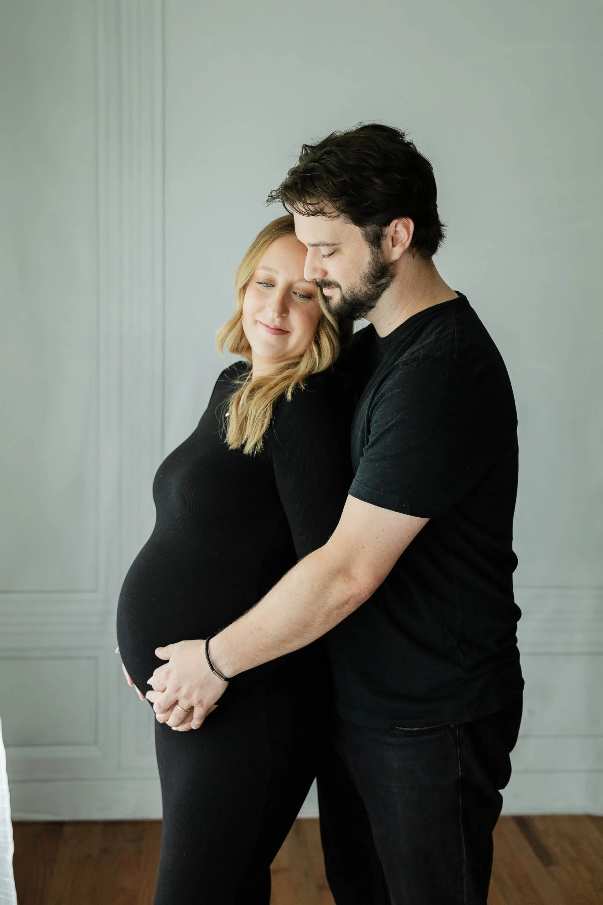 A husband gently holds his wife's pregnant belly as he embraces her