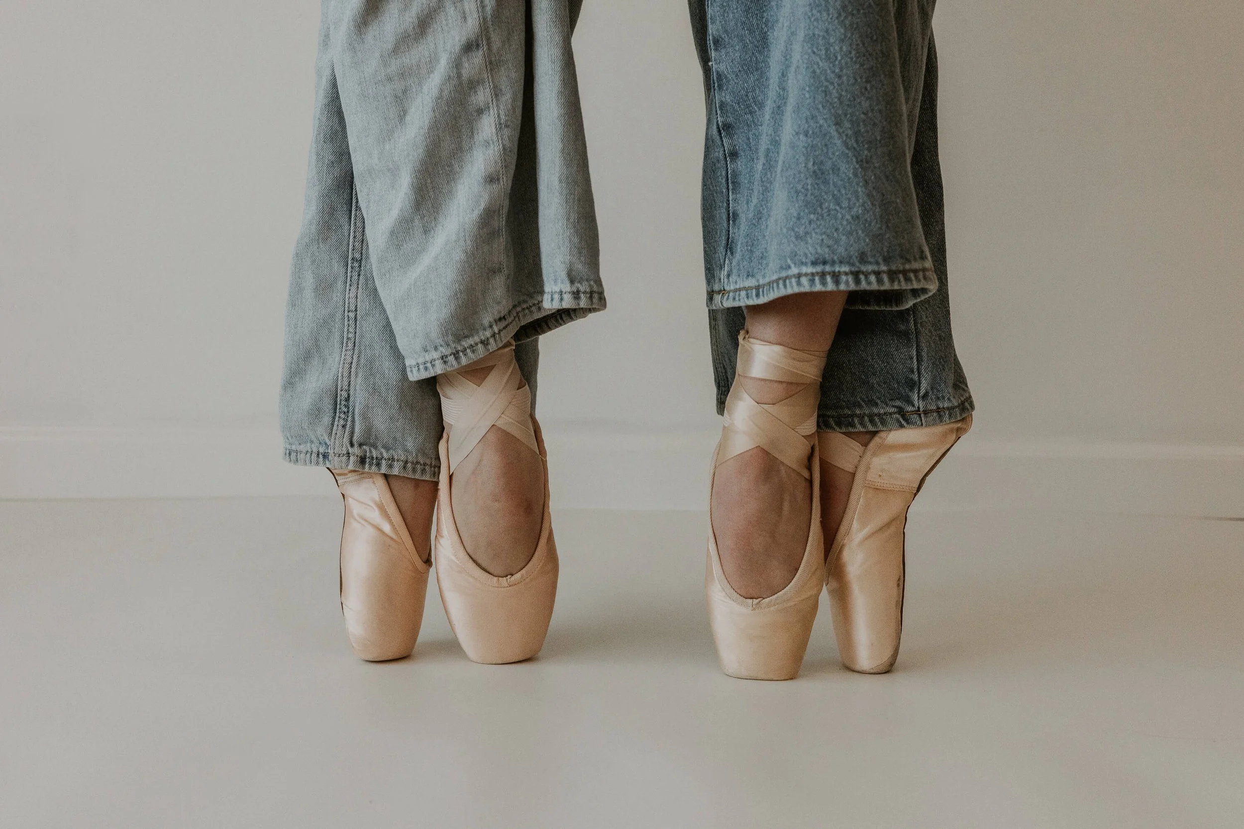 A closeup of two dancers' pointe shoes as they hold a pose.