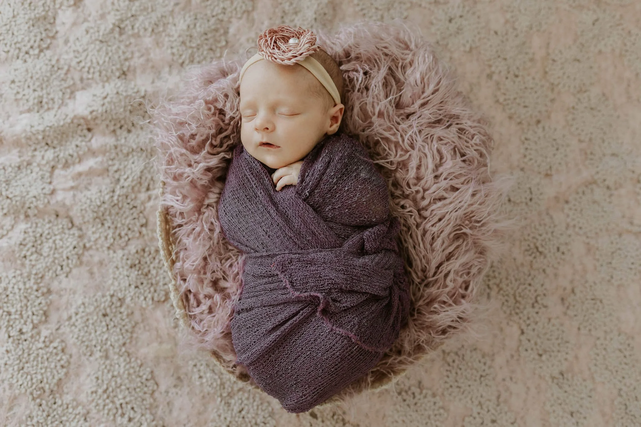 A newborn lays atop a a fluffy blanket in a basket during her studio session 