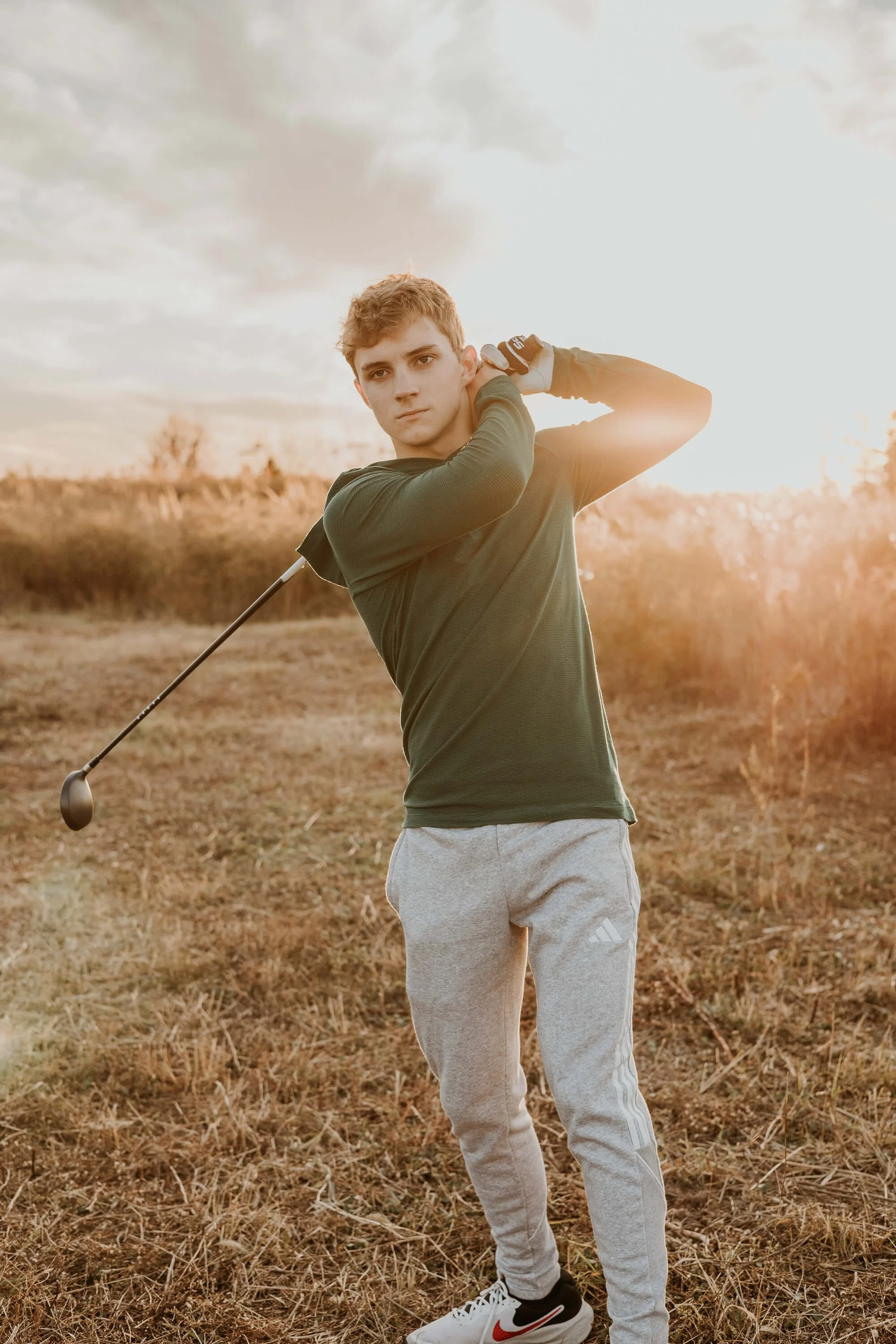 With sunset in the background, a teen boy holds a swing pose during his senior session in Bloomington IL