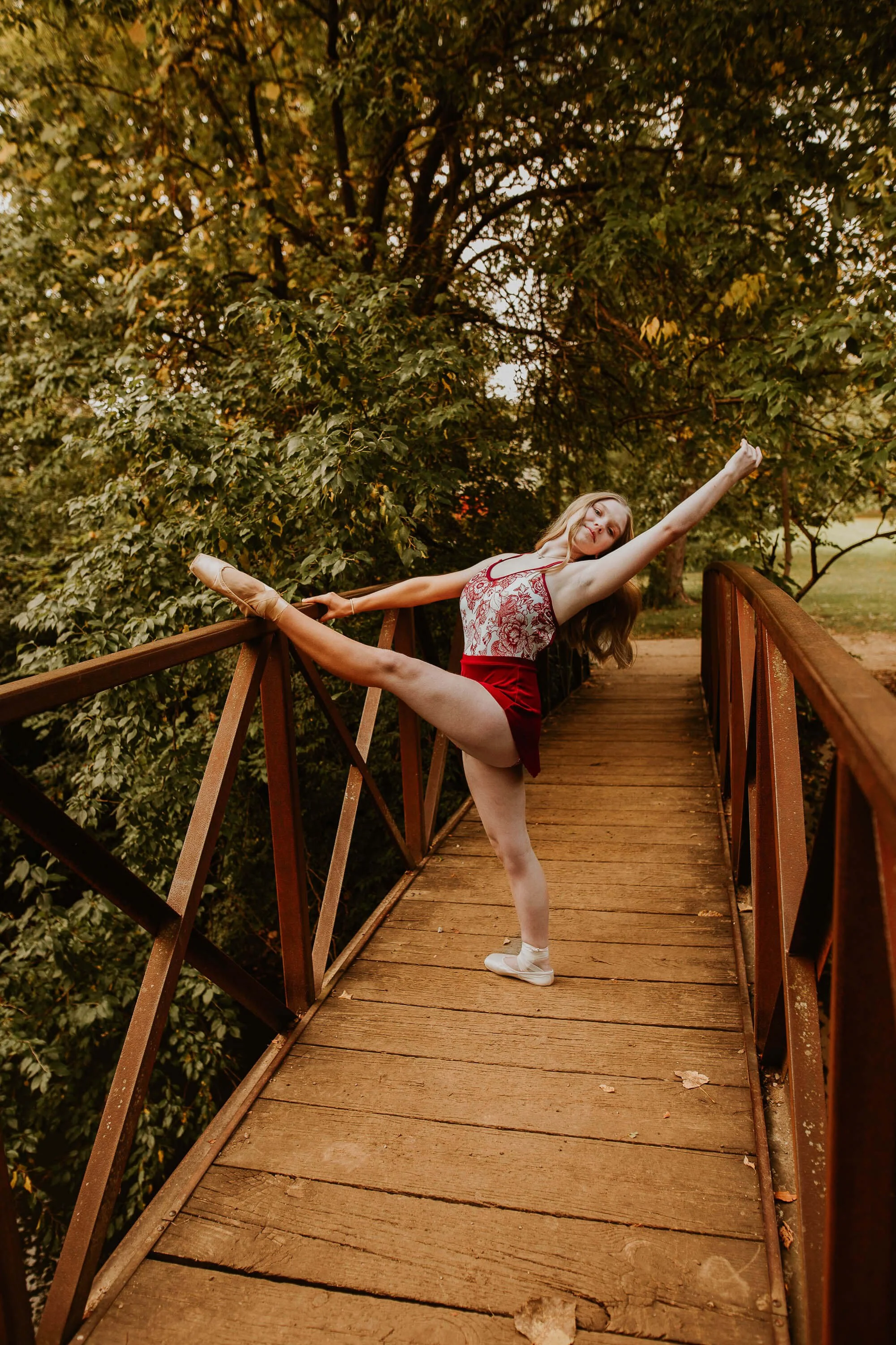 A ballerina from Twin Cities School of Dance holds her foot on the rail of a wooden bridge 