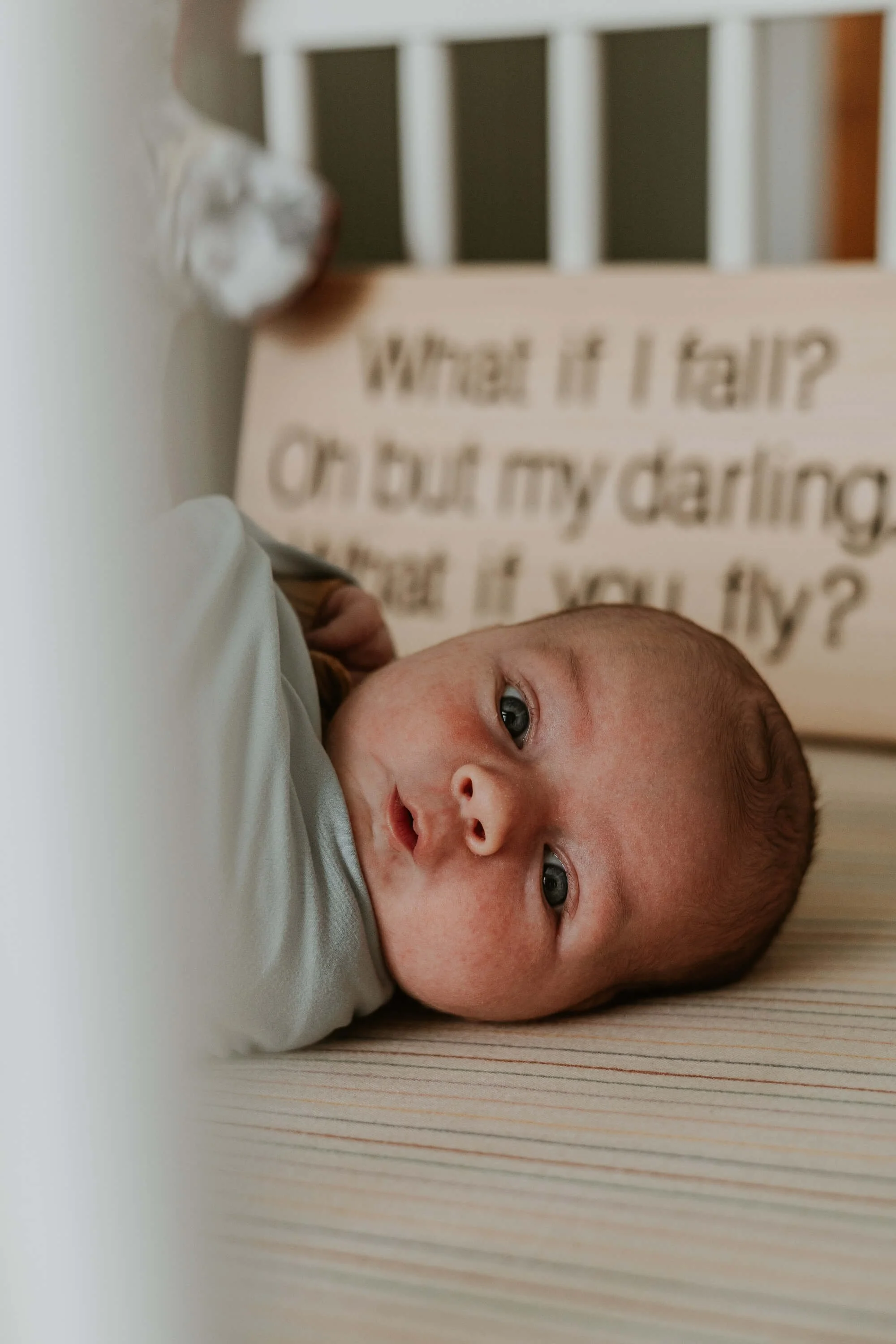 A close up of a wide-eyed newborn in his crib
