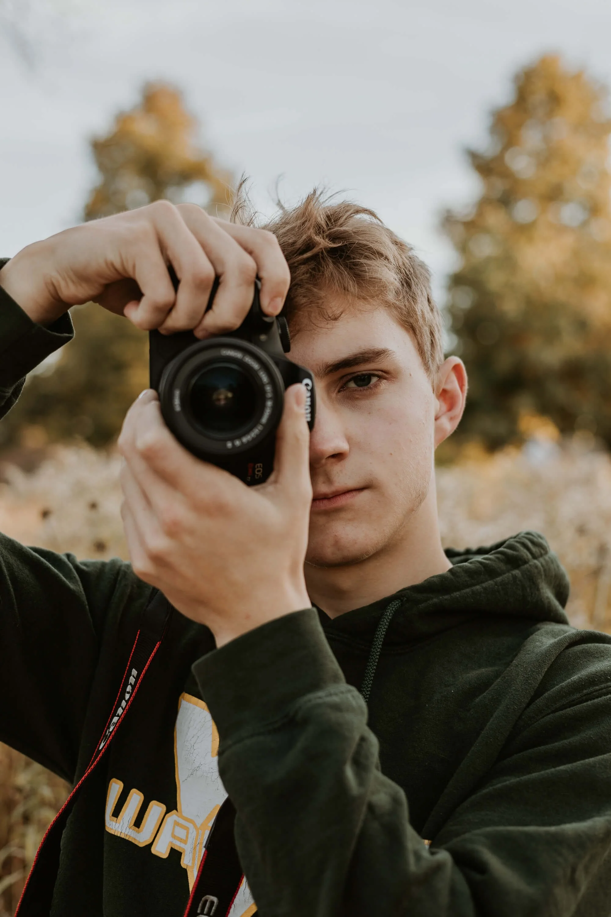 A high school senior holds his camera up to his eye.
