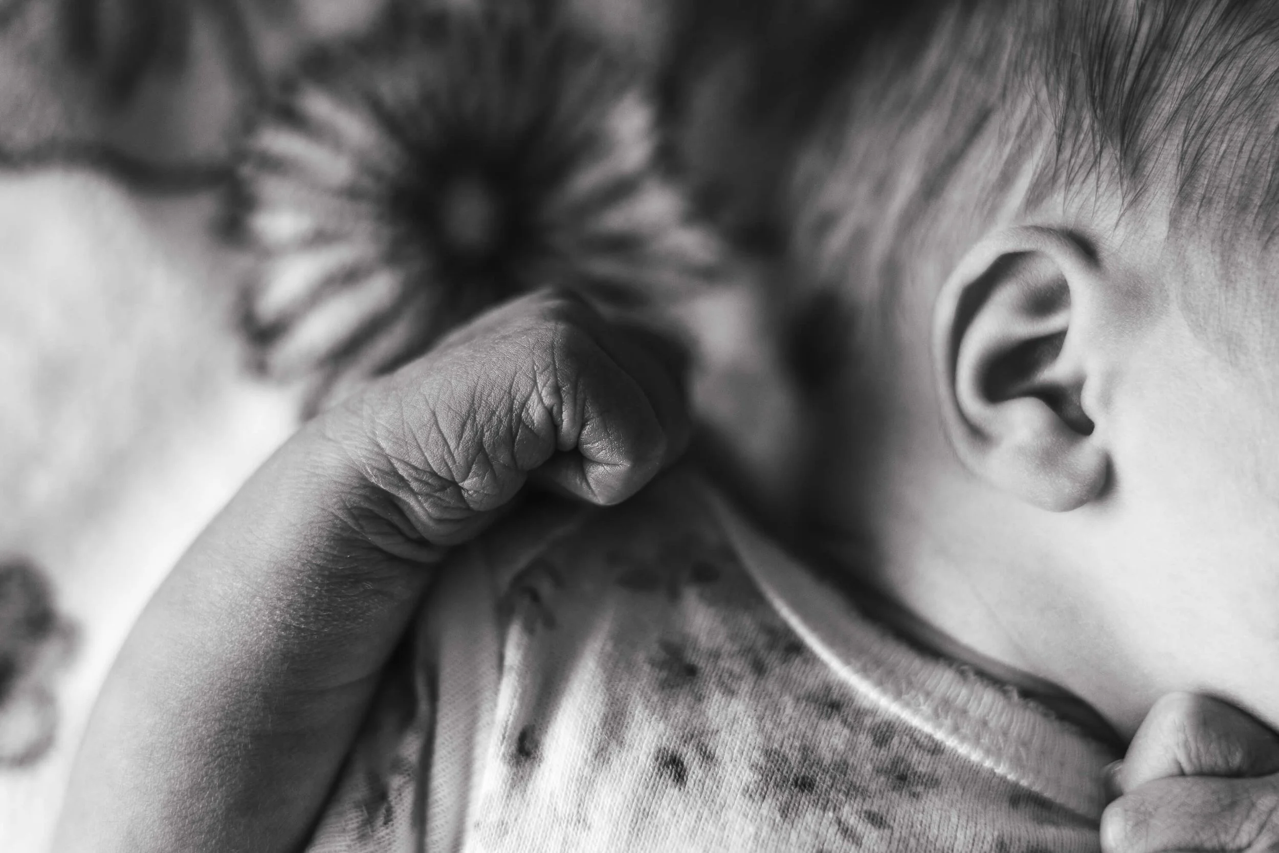 A newborn fist curled next to a sleeping baby's head