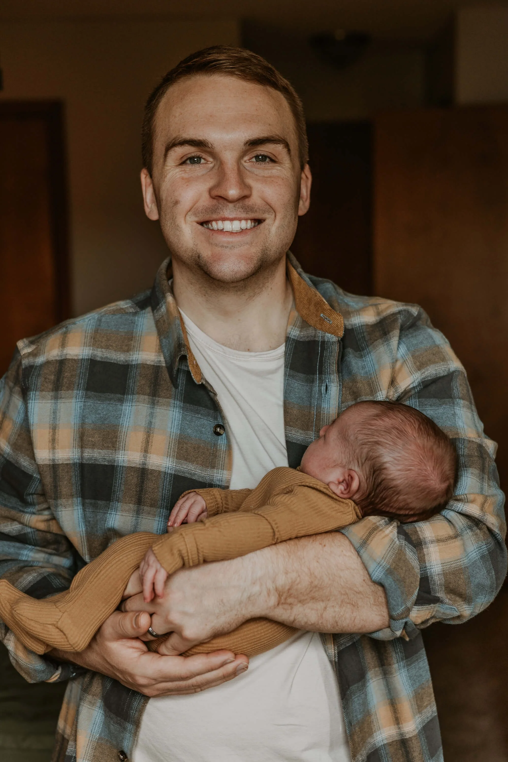 A new dad smiles widely while holding his new baby