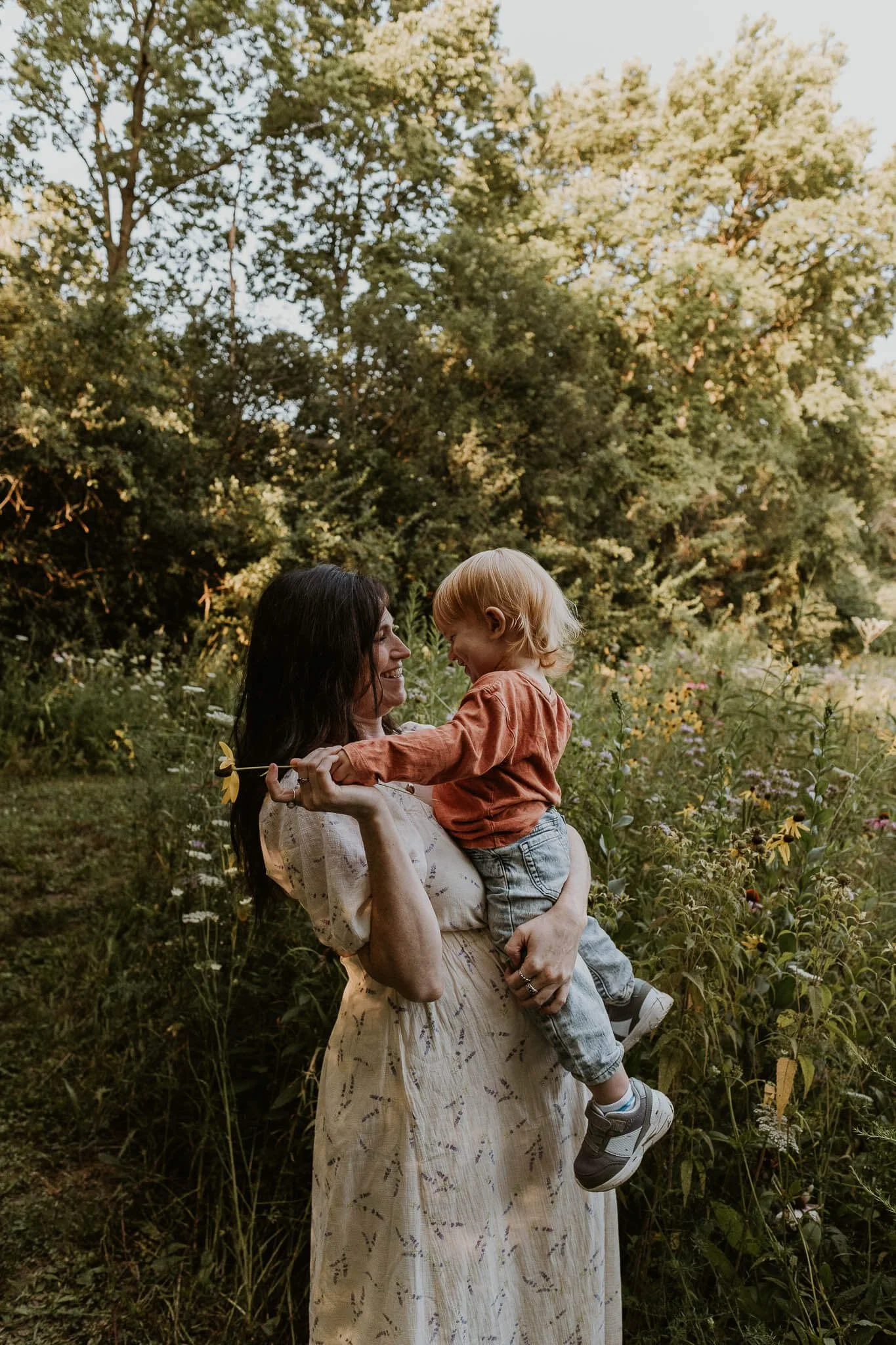 A mother looks lovingly at her toddler who sits upon her pregnant belly