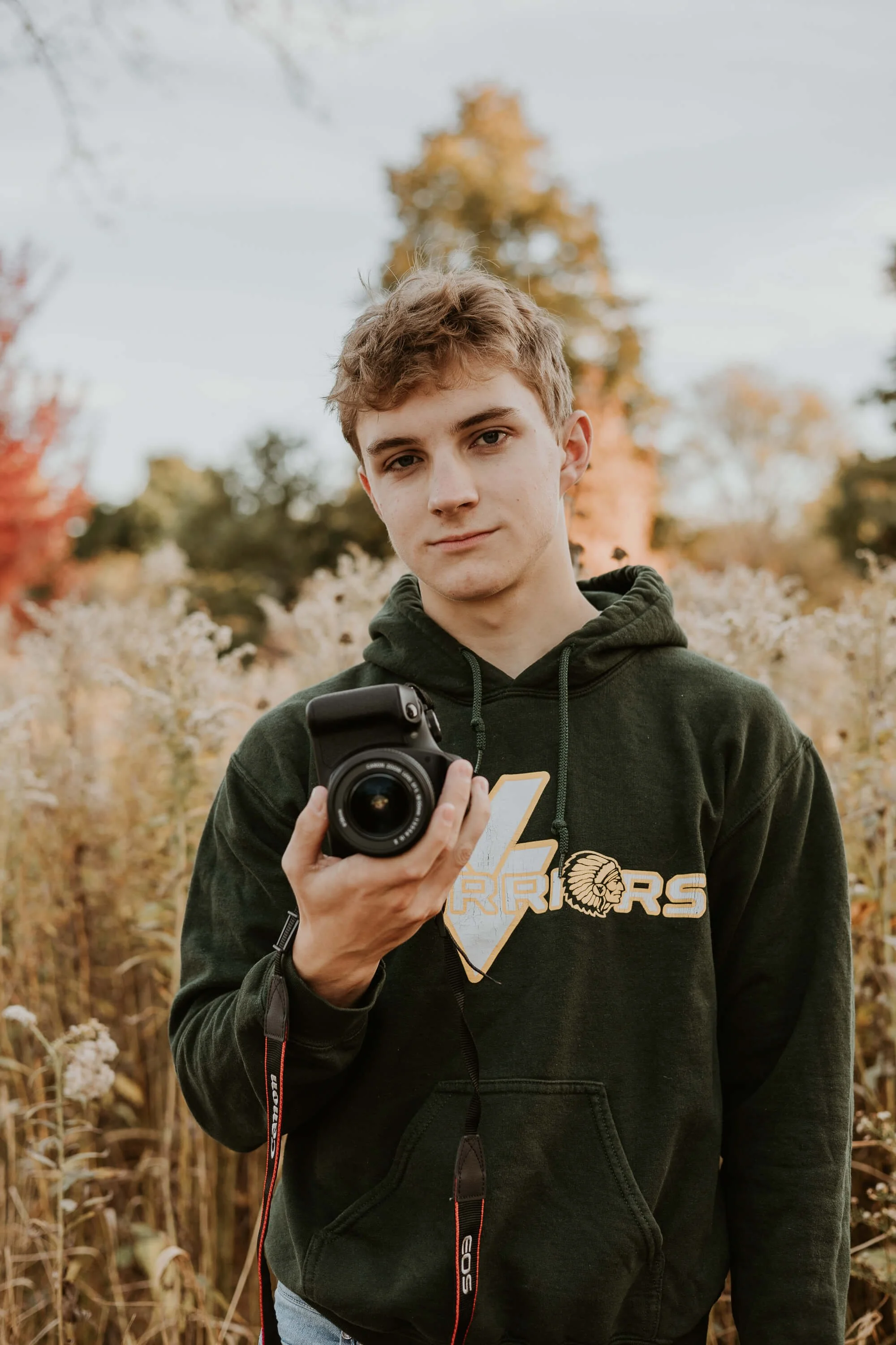 A teenage boy holds his camera at his chest in a field of prairie grass at Maxwell Park in Normal IL