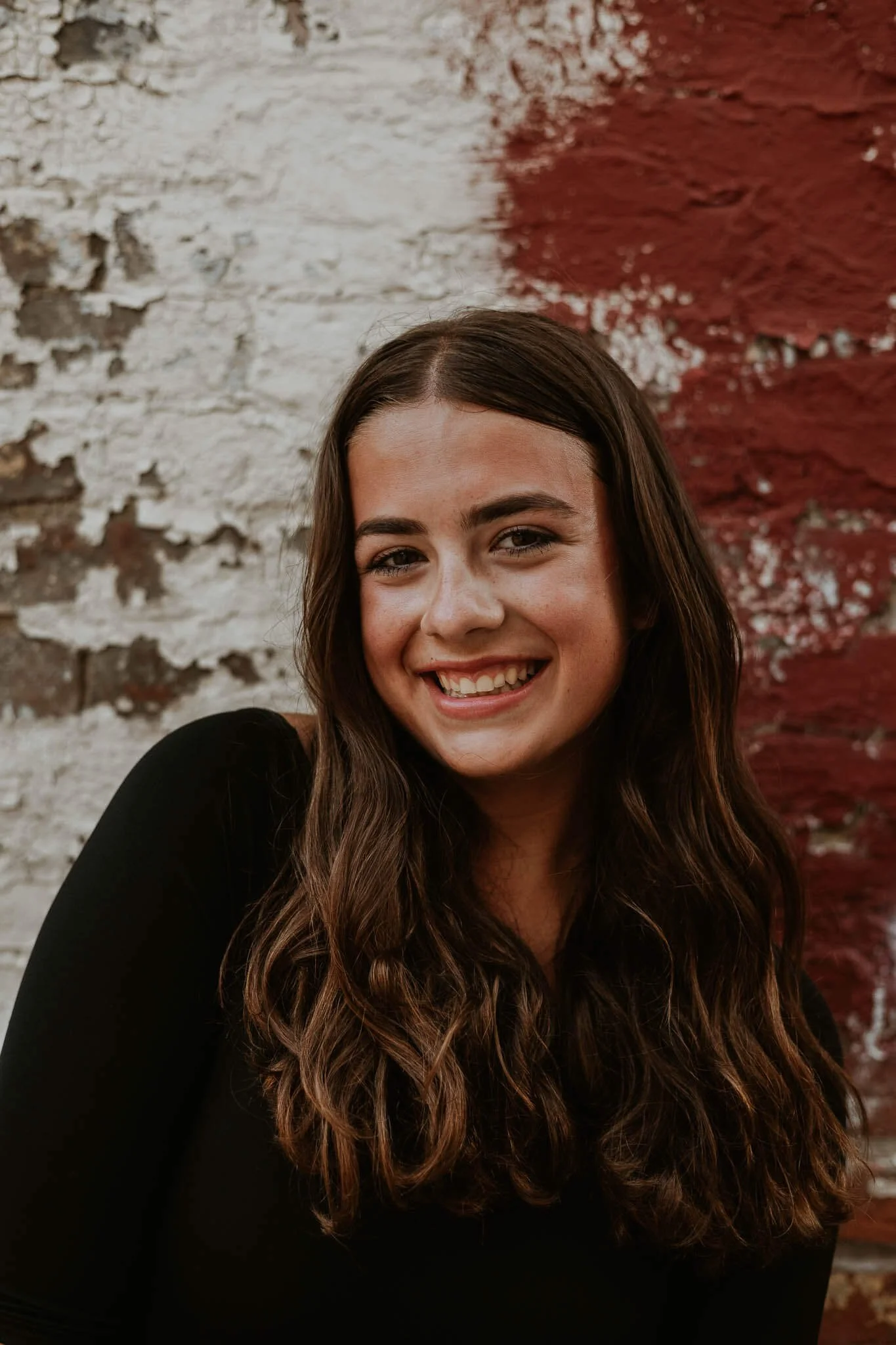A teen smiles brightly in front of a brick wall