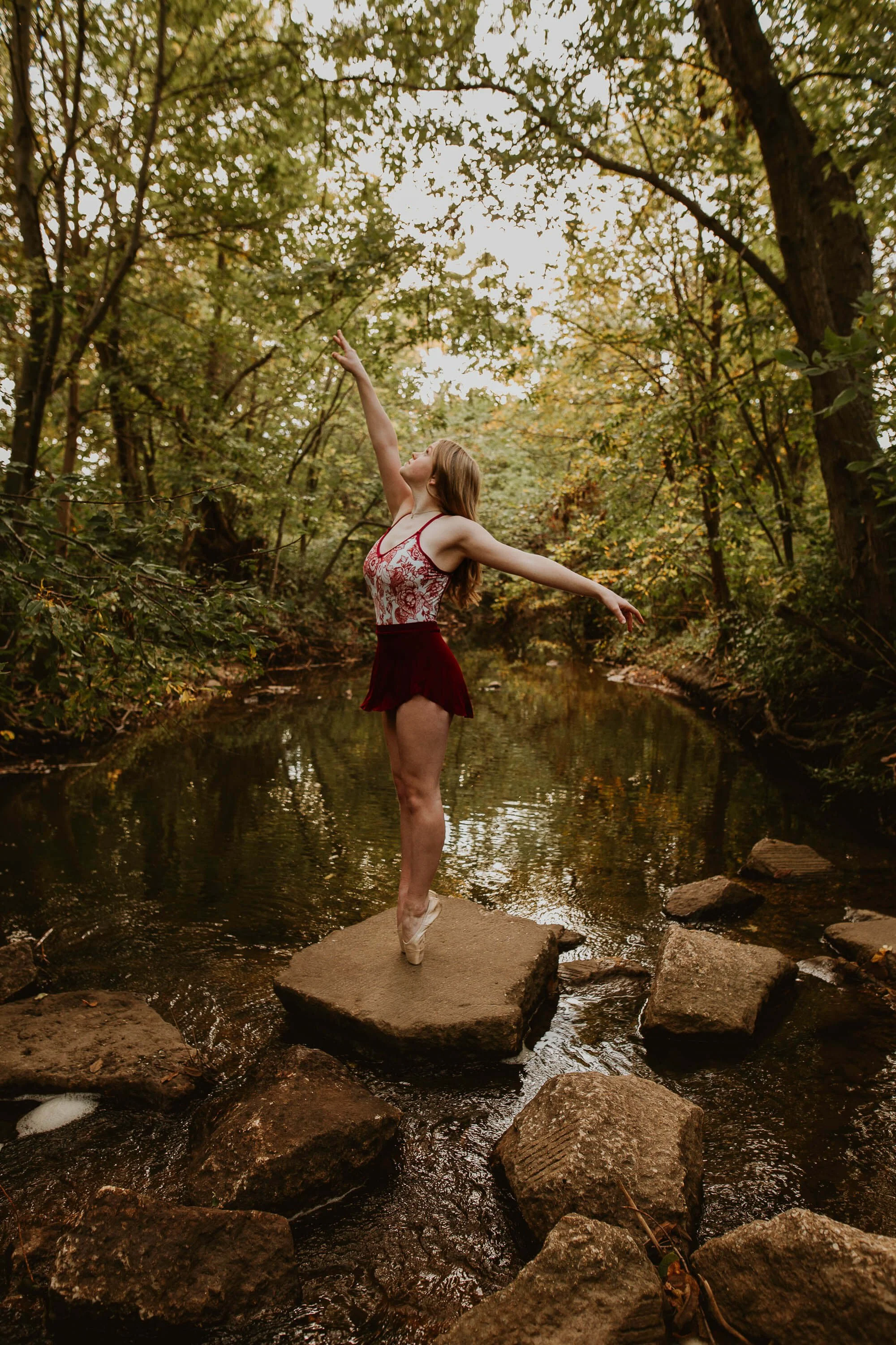 Senior dancer Katy stretches her hand above her head as she holds a pose en pointe at the creek near Ewing II park.