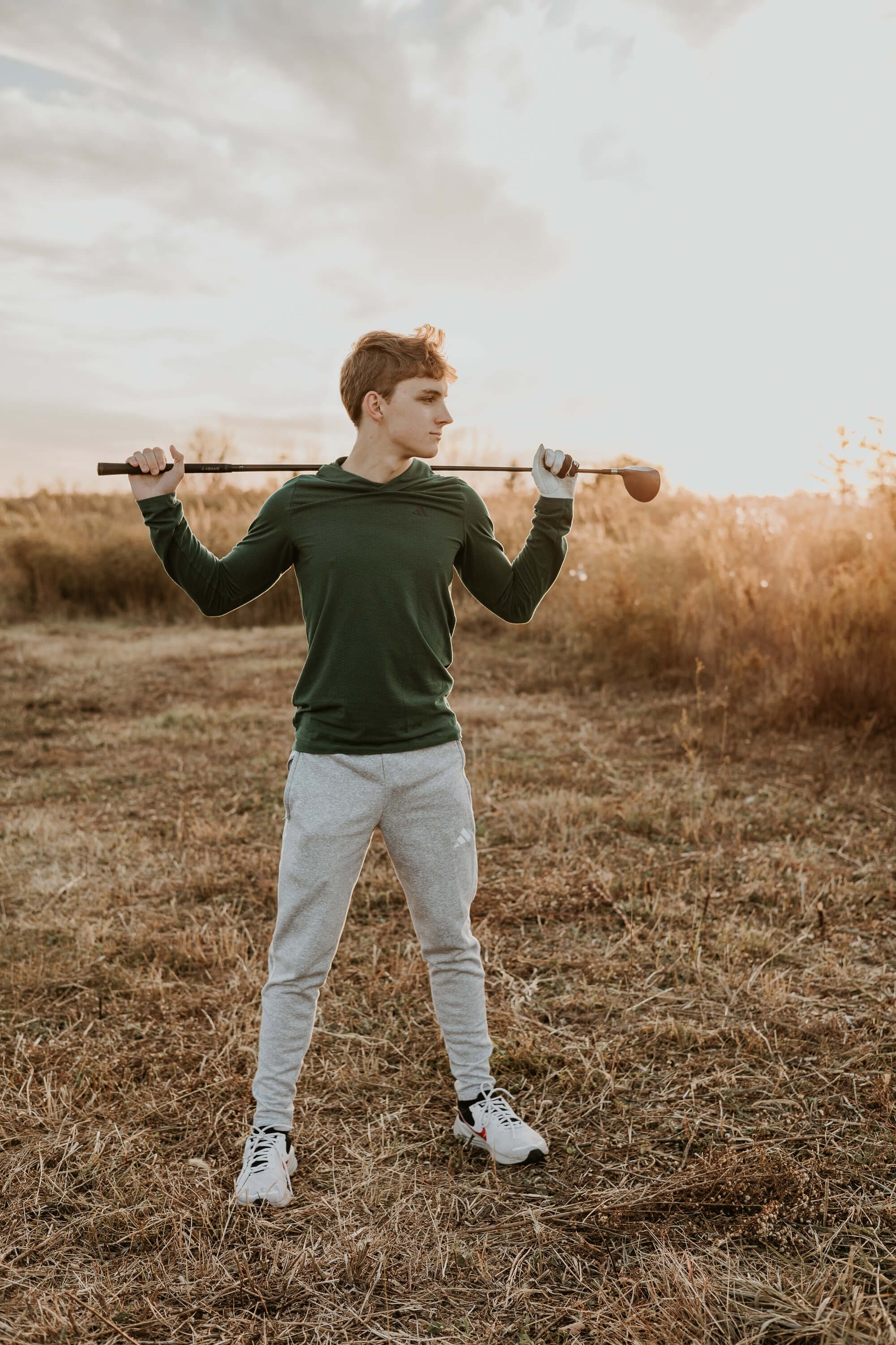 A senior holds his golf club across his shoulders at sunset atop the hill at Ewing II Park.