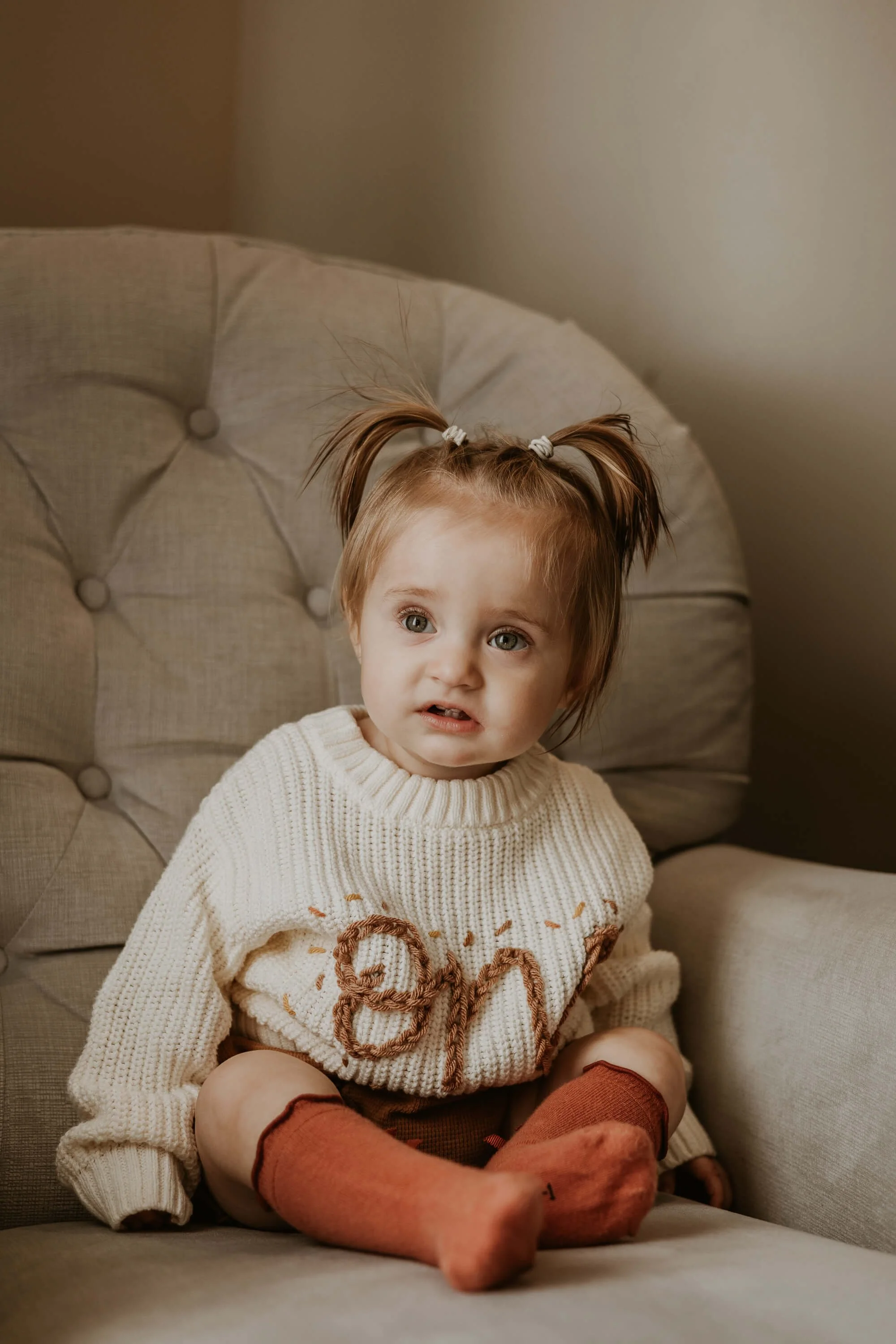 A 1 year old sits up in a plush rocking chair
