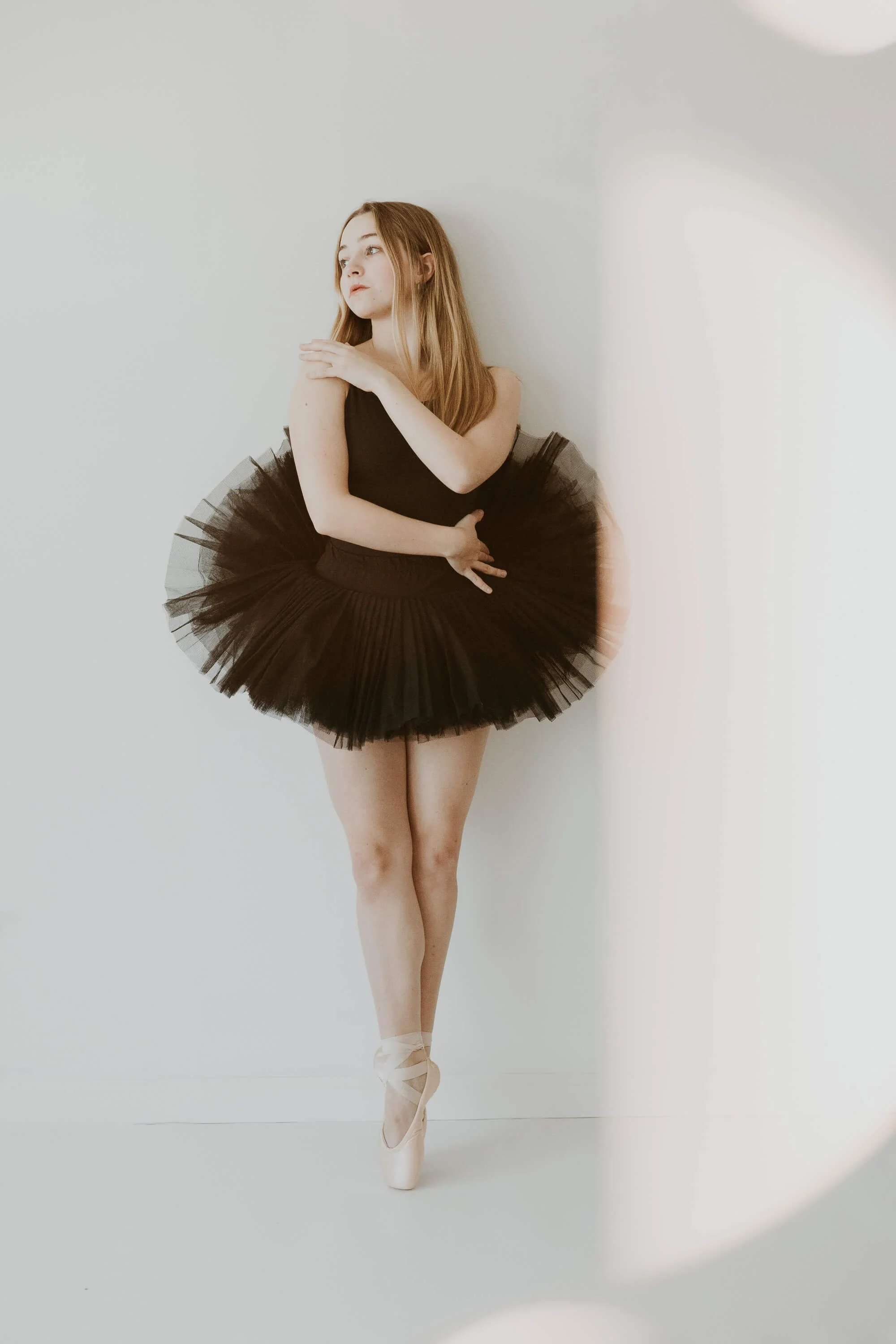 A high school girl holds a pose in first position en pointe.
