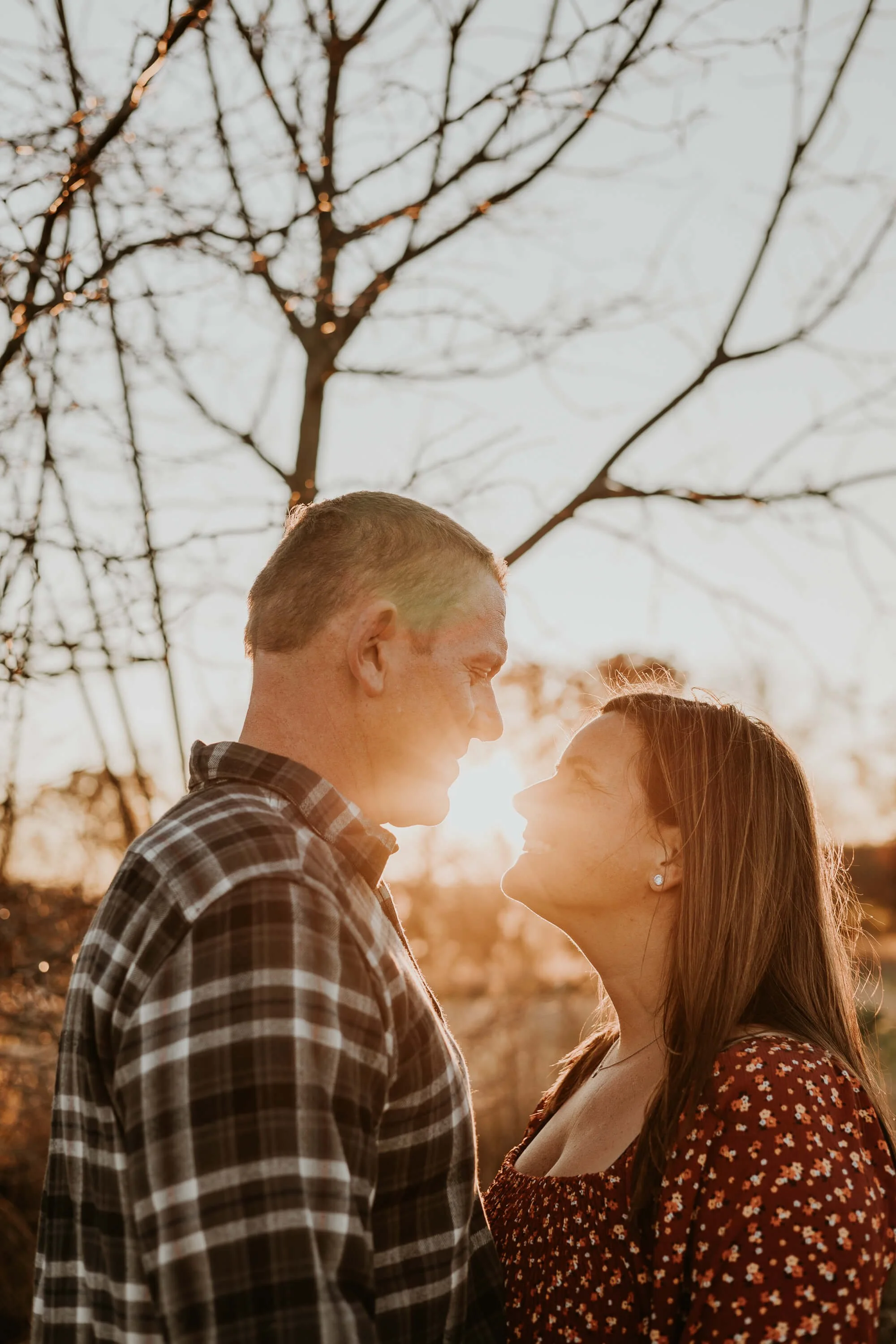The sunset peeks through a couple's close embrace, just before their lips meet in a kiss
