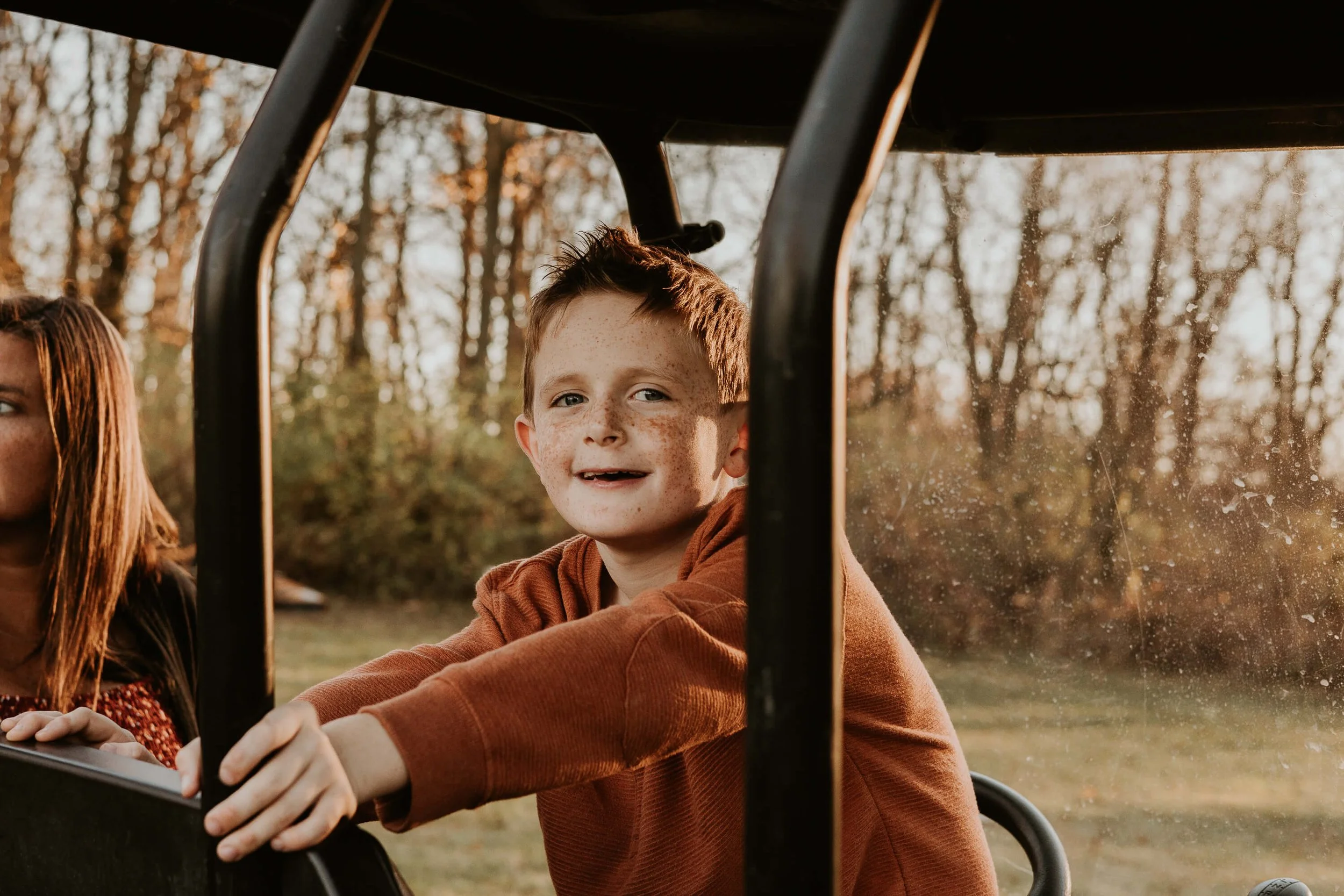 A freckle-faced boy smiles as he sits in the back of his parent's golf cart