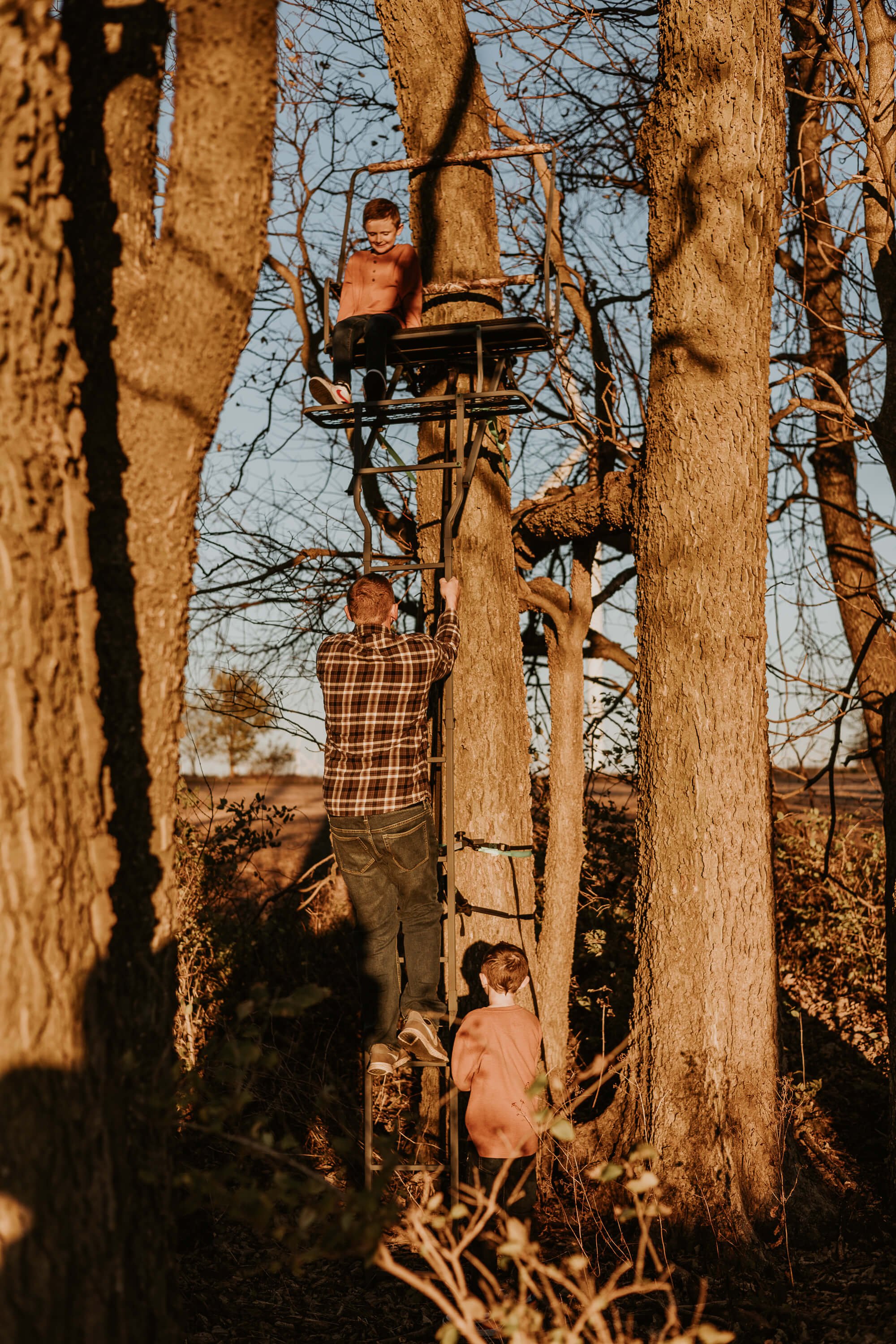A father assists his son's as they climb up to their deer stand