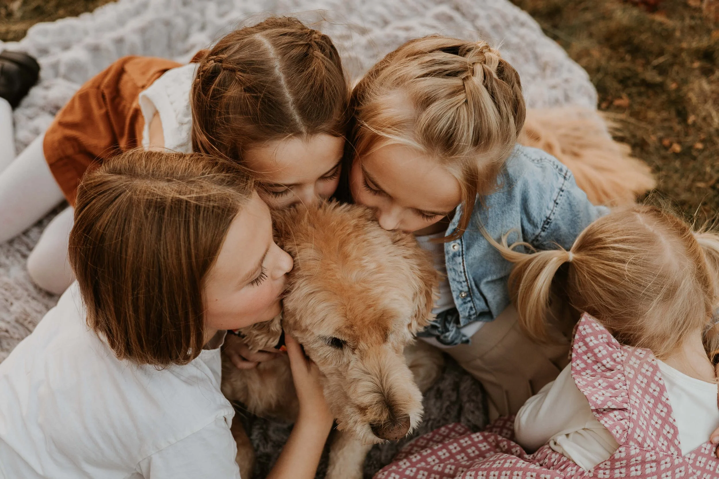 Four sisters sit closely to their aging dog, kissing his head.