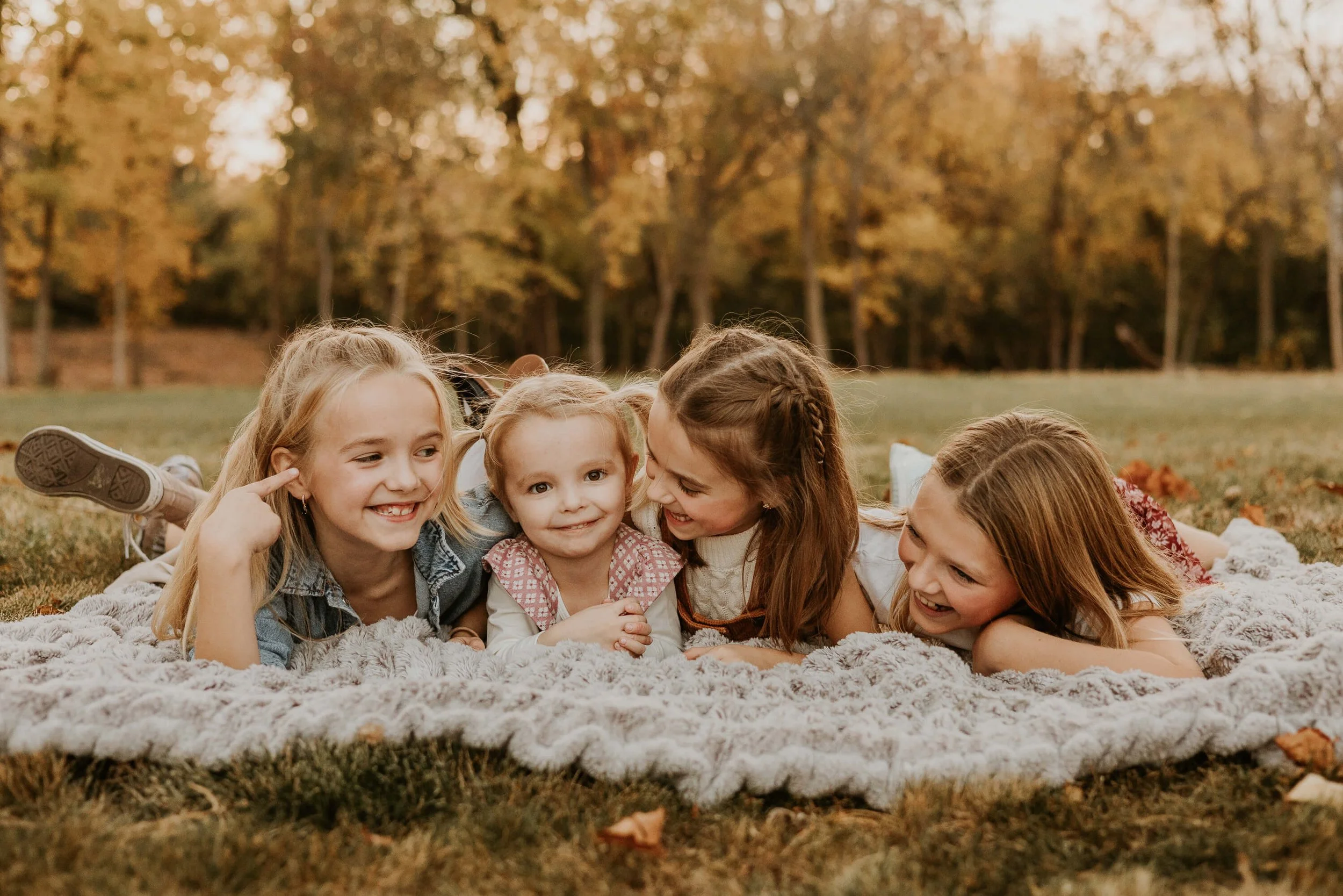 four sisters giggle and smile at each other as they lay on a blanket in their backyard