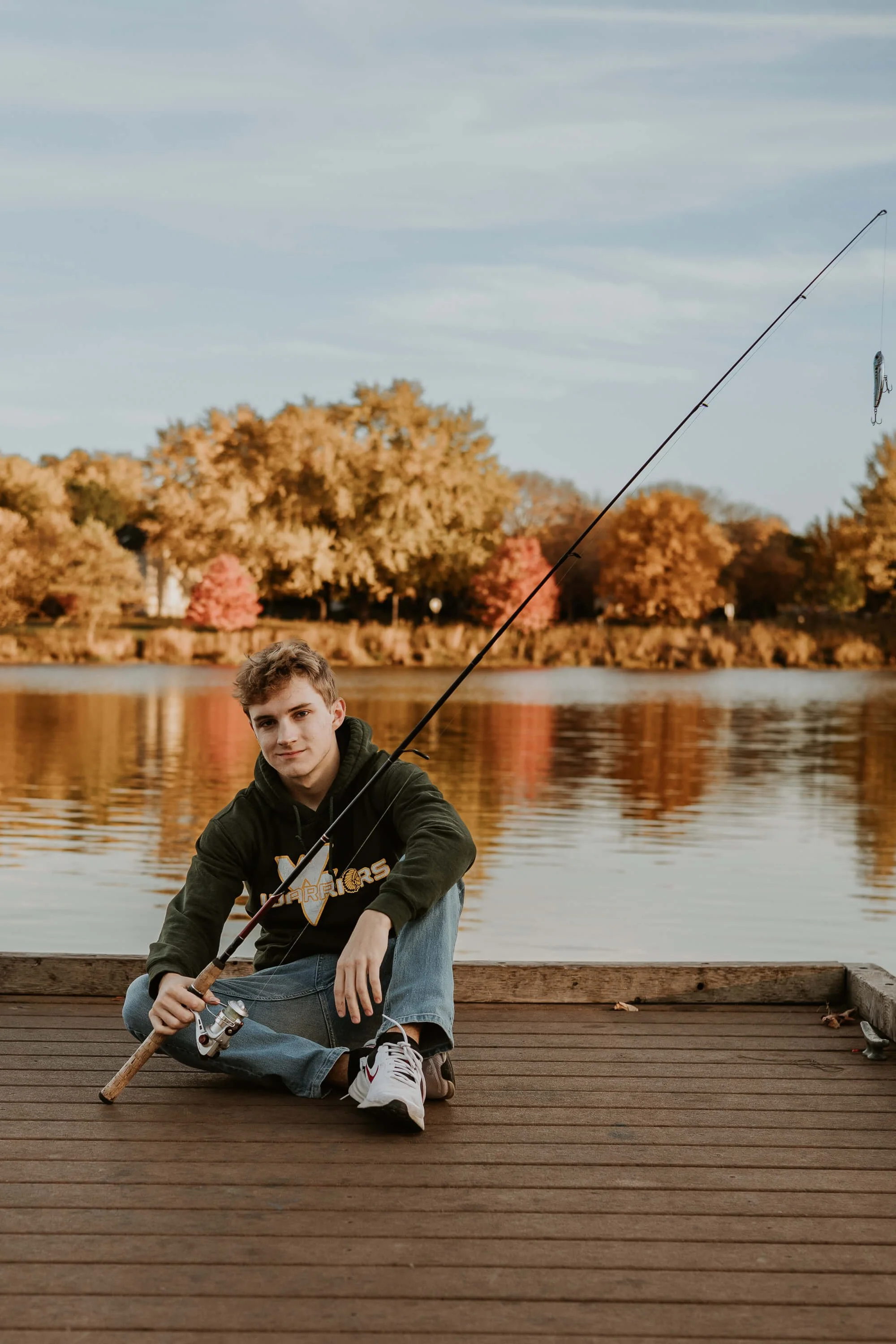 A high school boy holds his fishing pole as he sits on a dock at Lake Bloomington