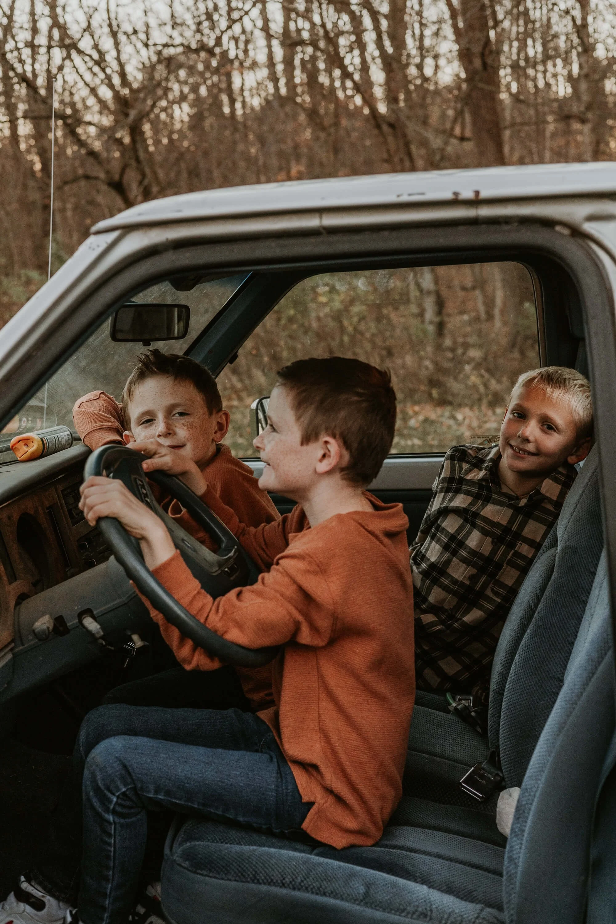 A twin and his two brothers pretend to drive in the cab of an old pick up truck
