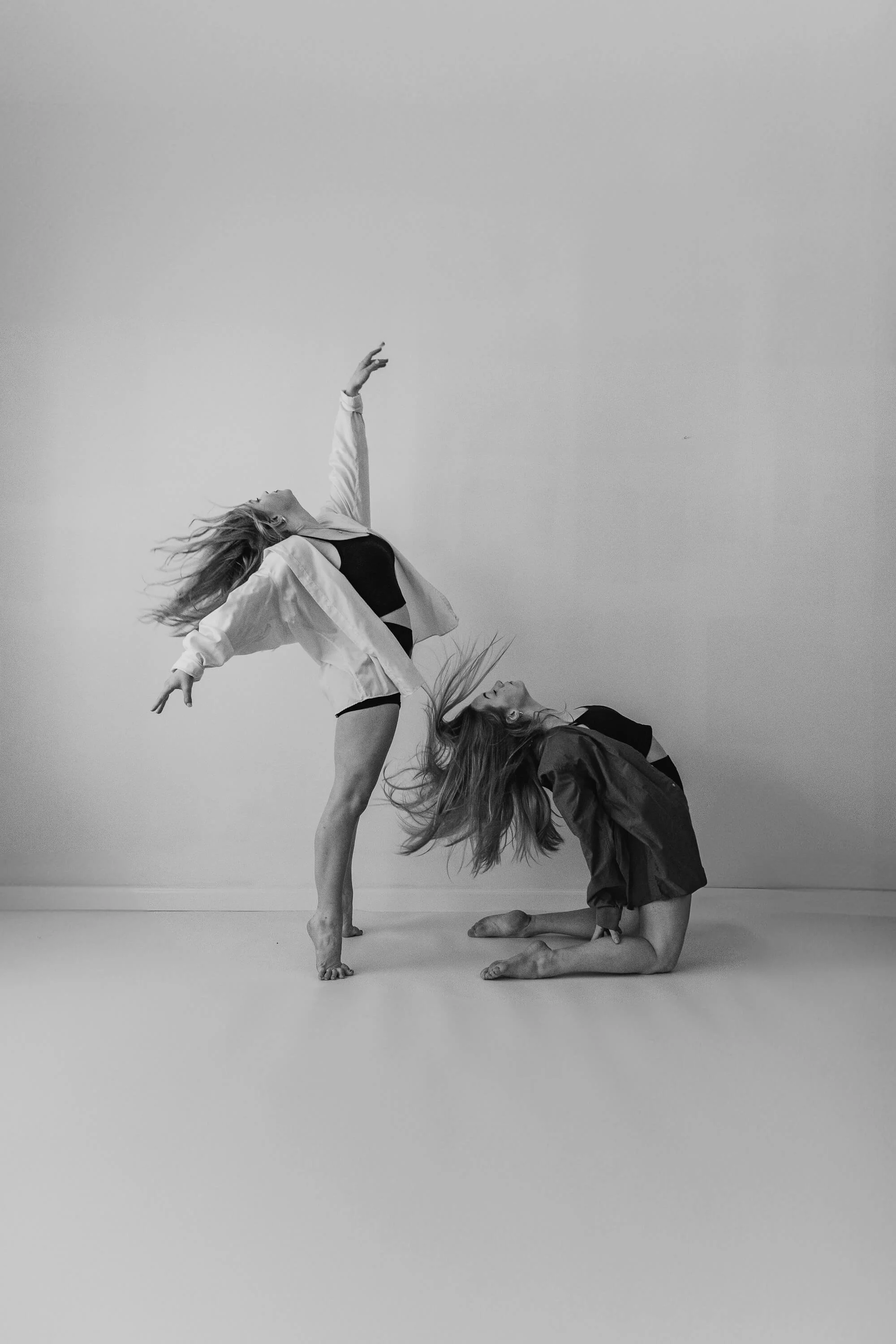 A black and white image of two dancers posing as they throw their heads back to splay out their hair.