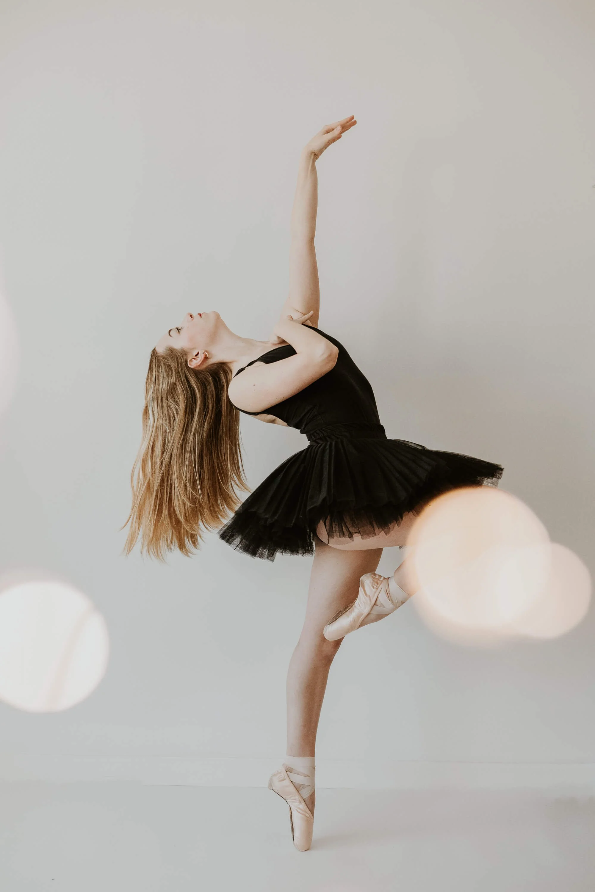A pose en pointe, balancing on one foot, with the other gently placed at her knee, arms above her.