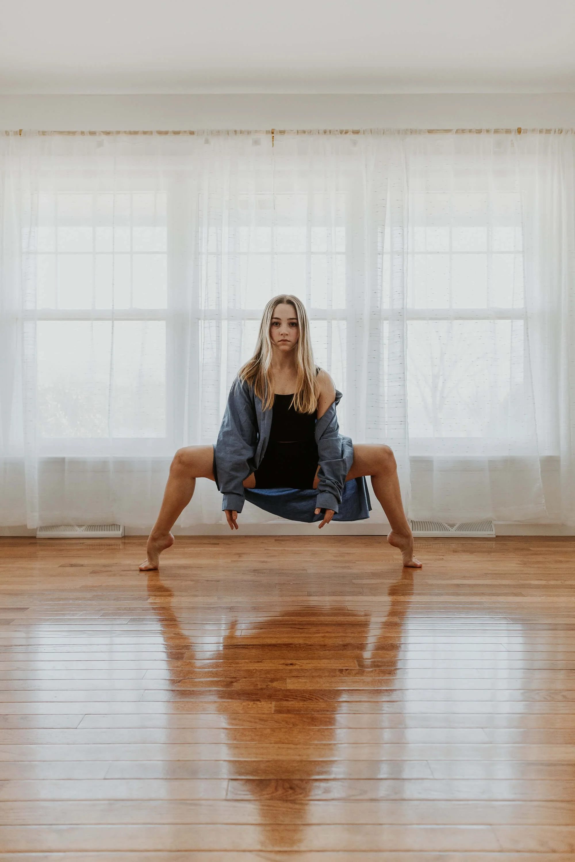 A dancer dressed in an oversized blue button down shirt holds second on tip toe.