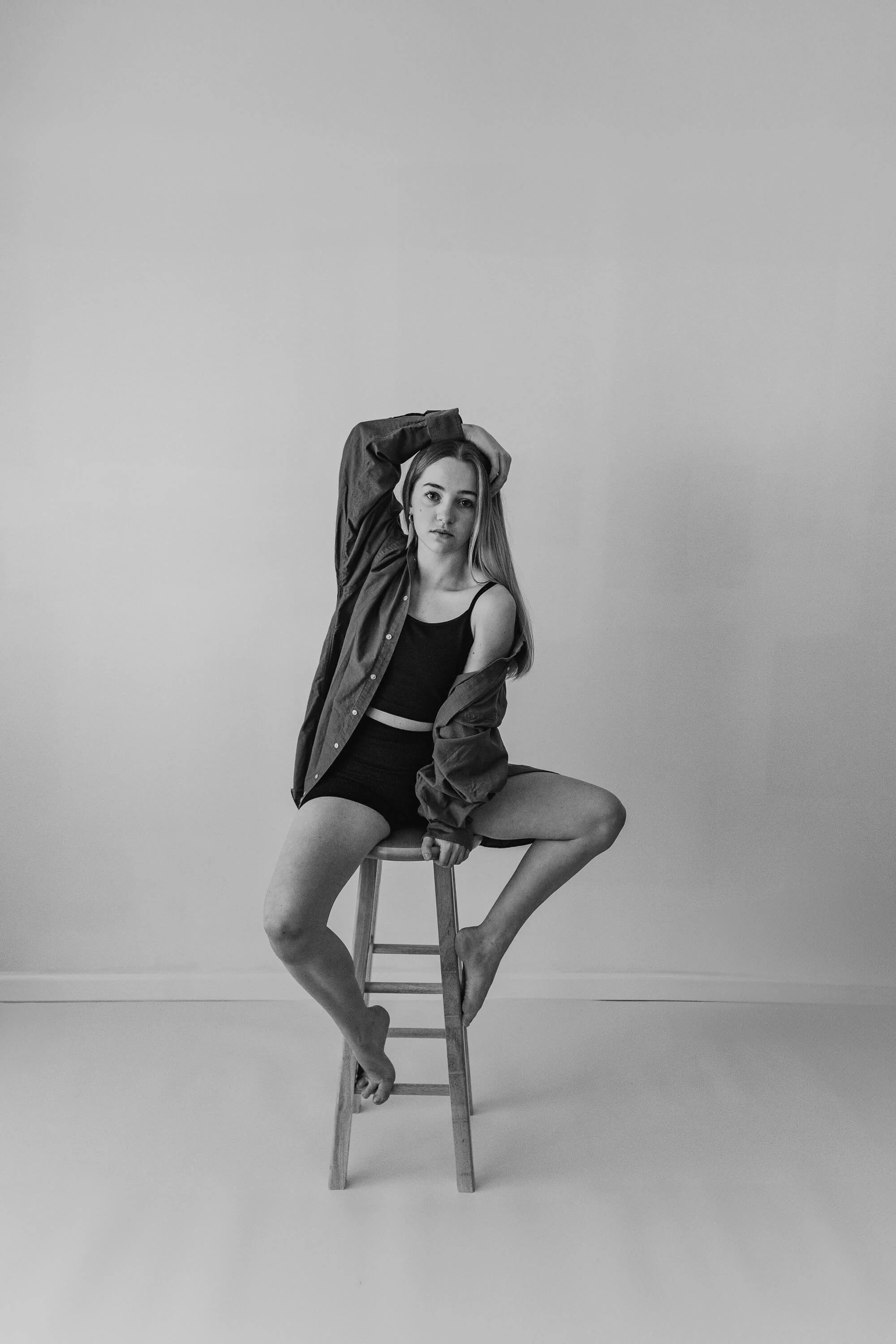 A black and white image of a dancer sitting comfortably atop a stool during her studio session in Bloomington, IL