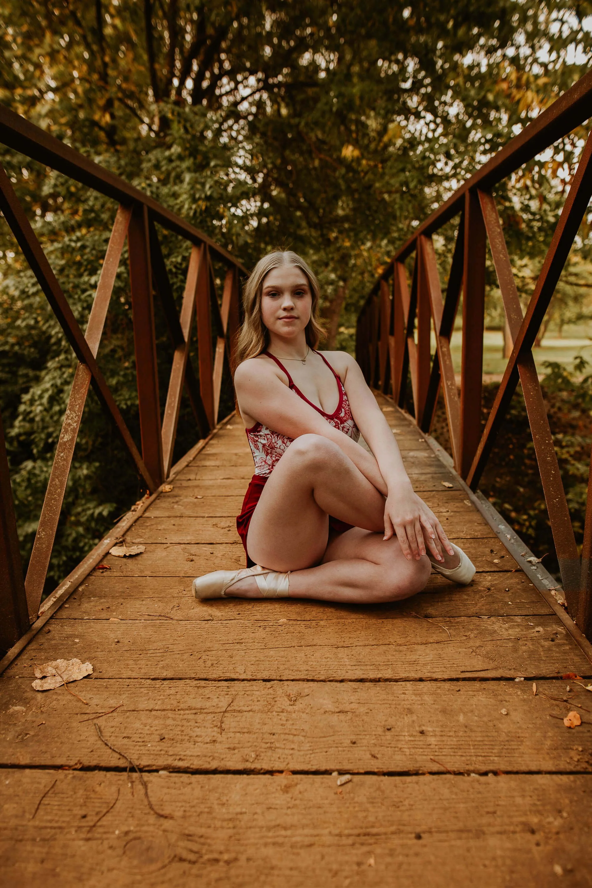 A ballerina sits upright, legs crossed in a strong pose atop a wooden bridge at Ewing Park