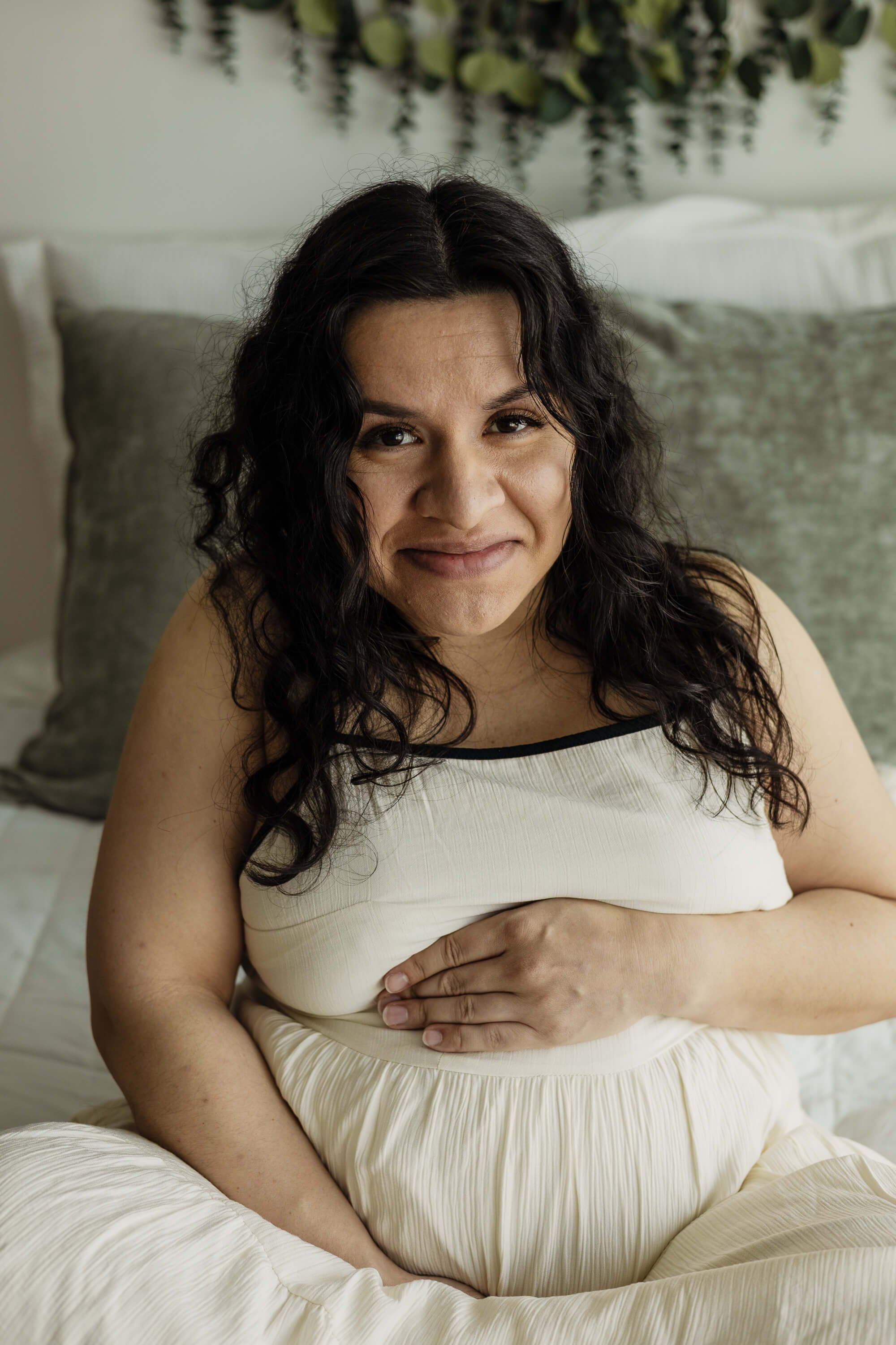 A pregnant mom smiles softly while sitting on a bed, holding her belly
