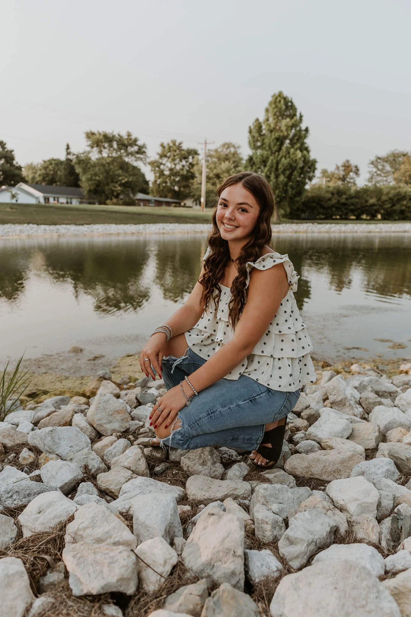 A senior at Olympia High School crouches in a comfortable position atop some decorative rocks near a pond.