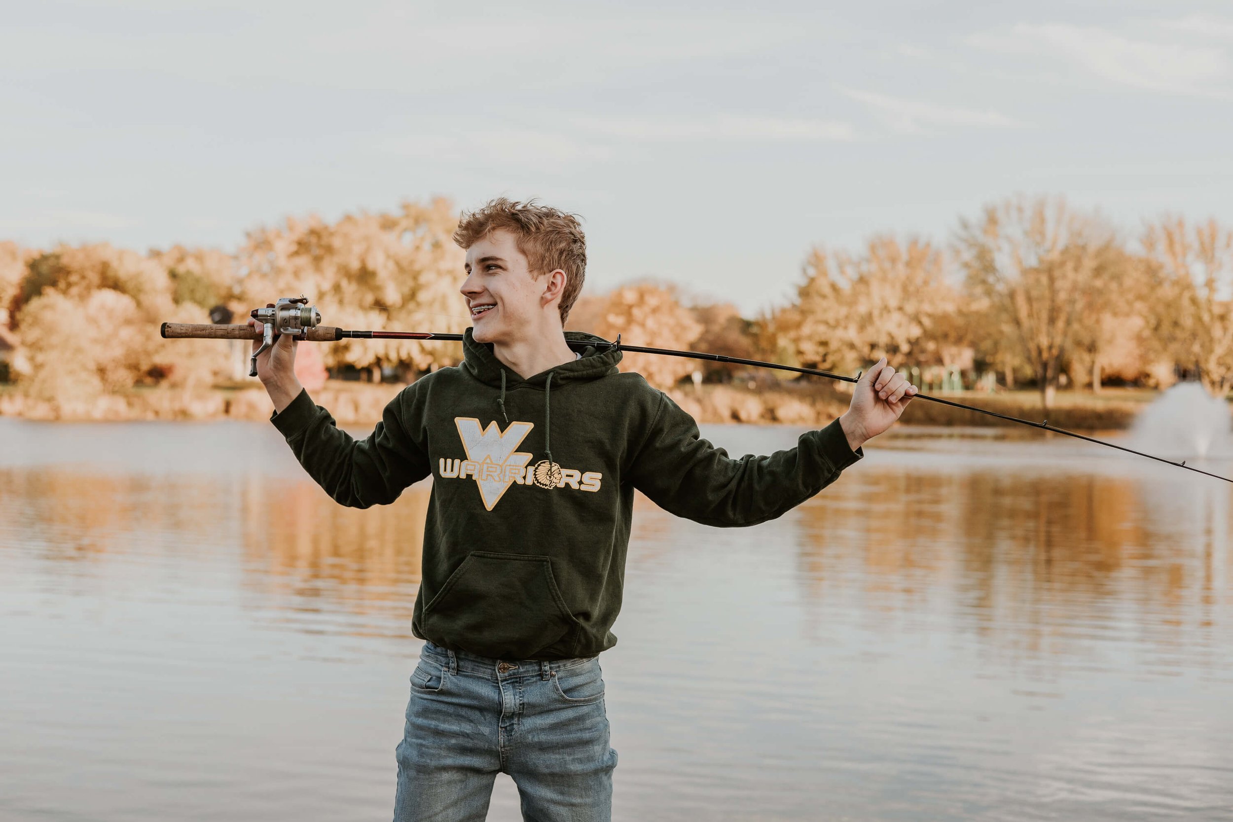 A high school senioir laughs as he holds his fishing pole across his shoulders