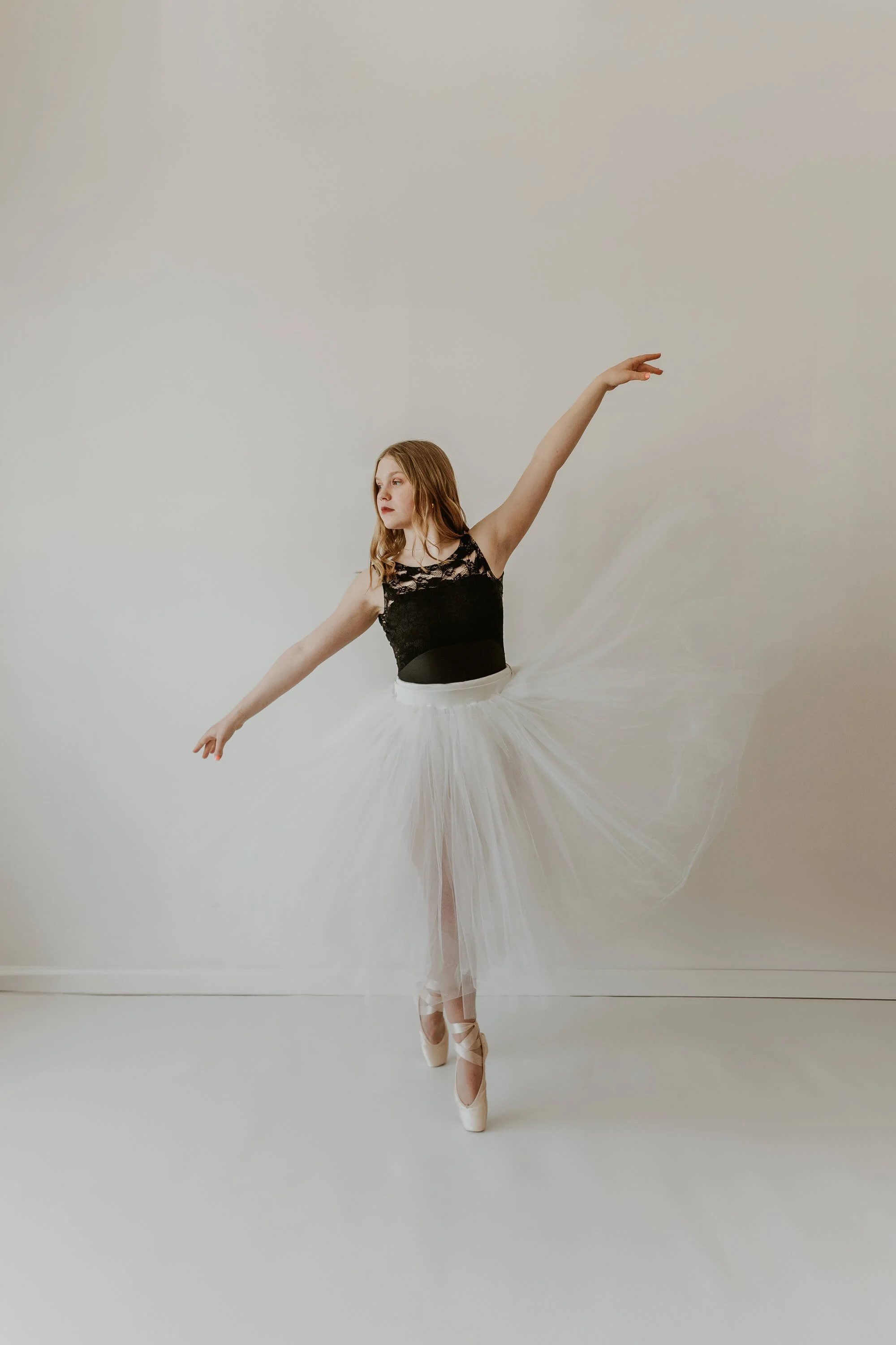 A high school dancer wearing a white tutu holds a pose with both feet en pointe, arms gracefully stretched out.