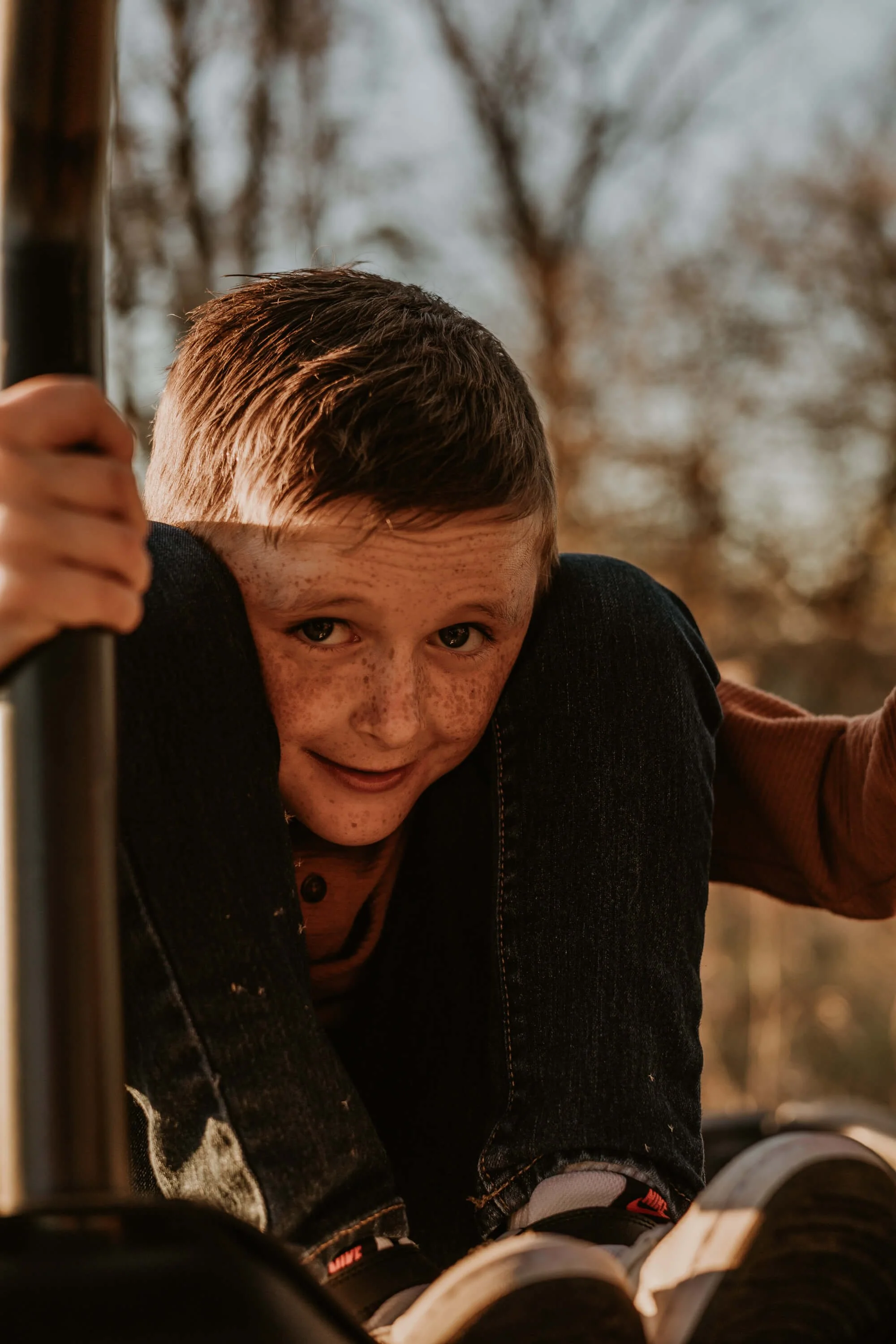 A young boy sits awkwardly with a silly grin on his face, knees pulled up to his ears.