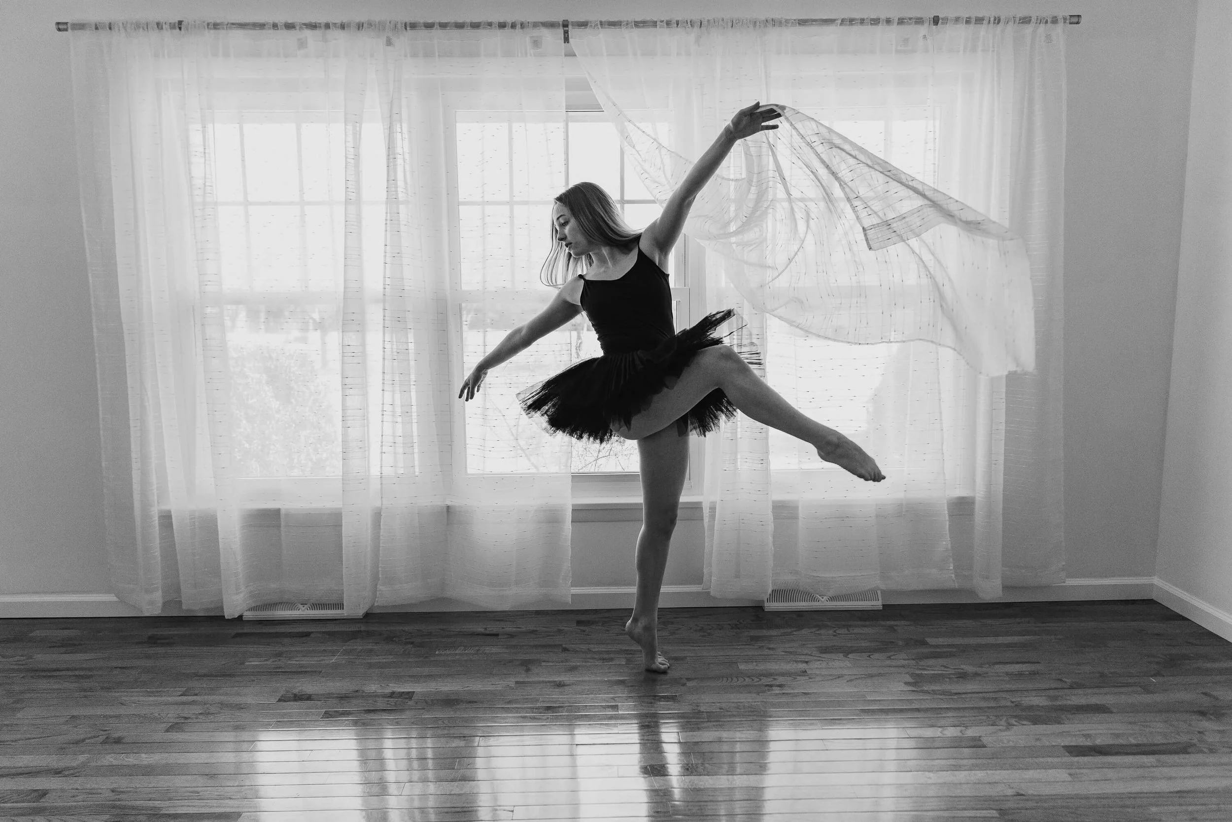 Black and white image of a dancer playing with sheer curtains as she dances.
