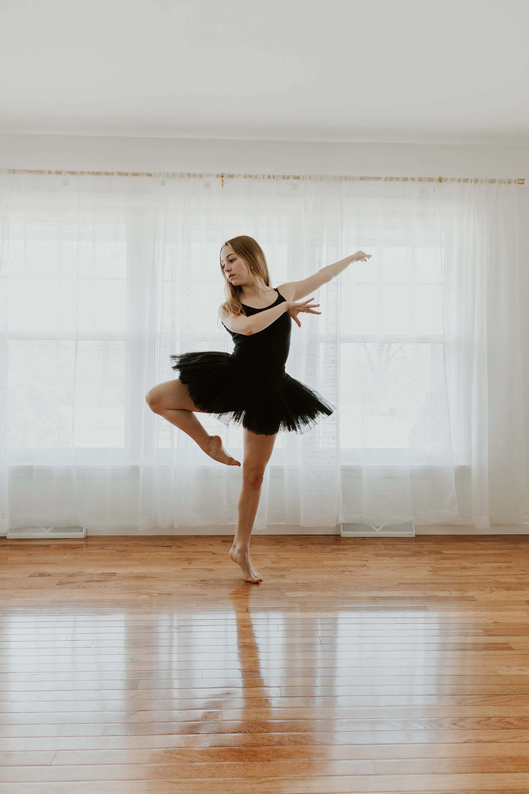 A ballet dancer dressed in a black tutu and leotard holds a pose in a studio in Bloomington, IL