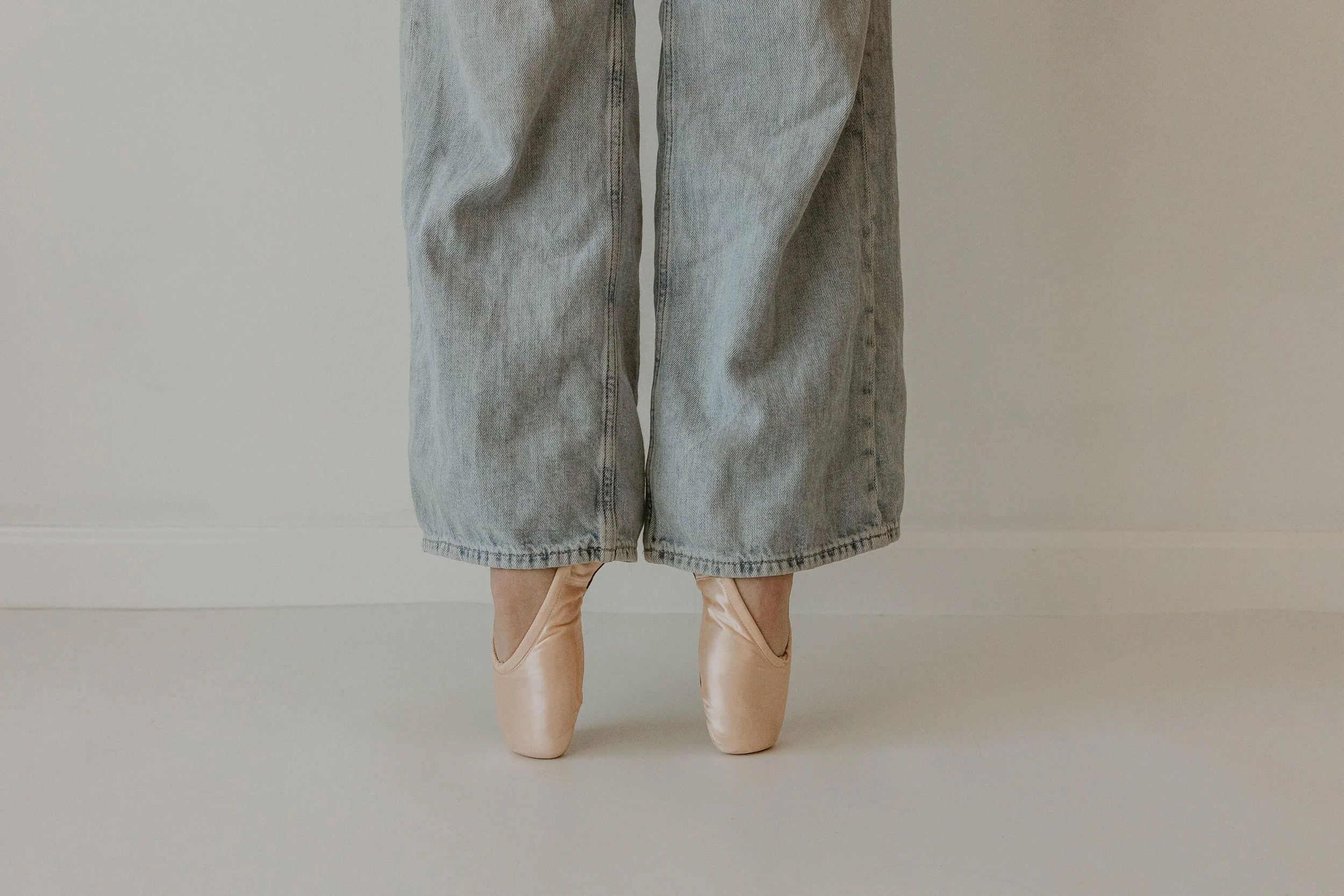 A ballerina wearing jeans and pointe shoes holds first position.