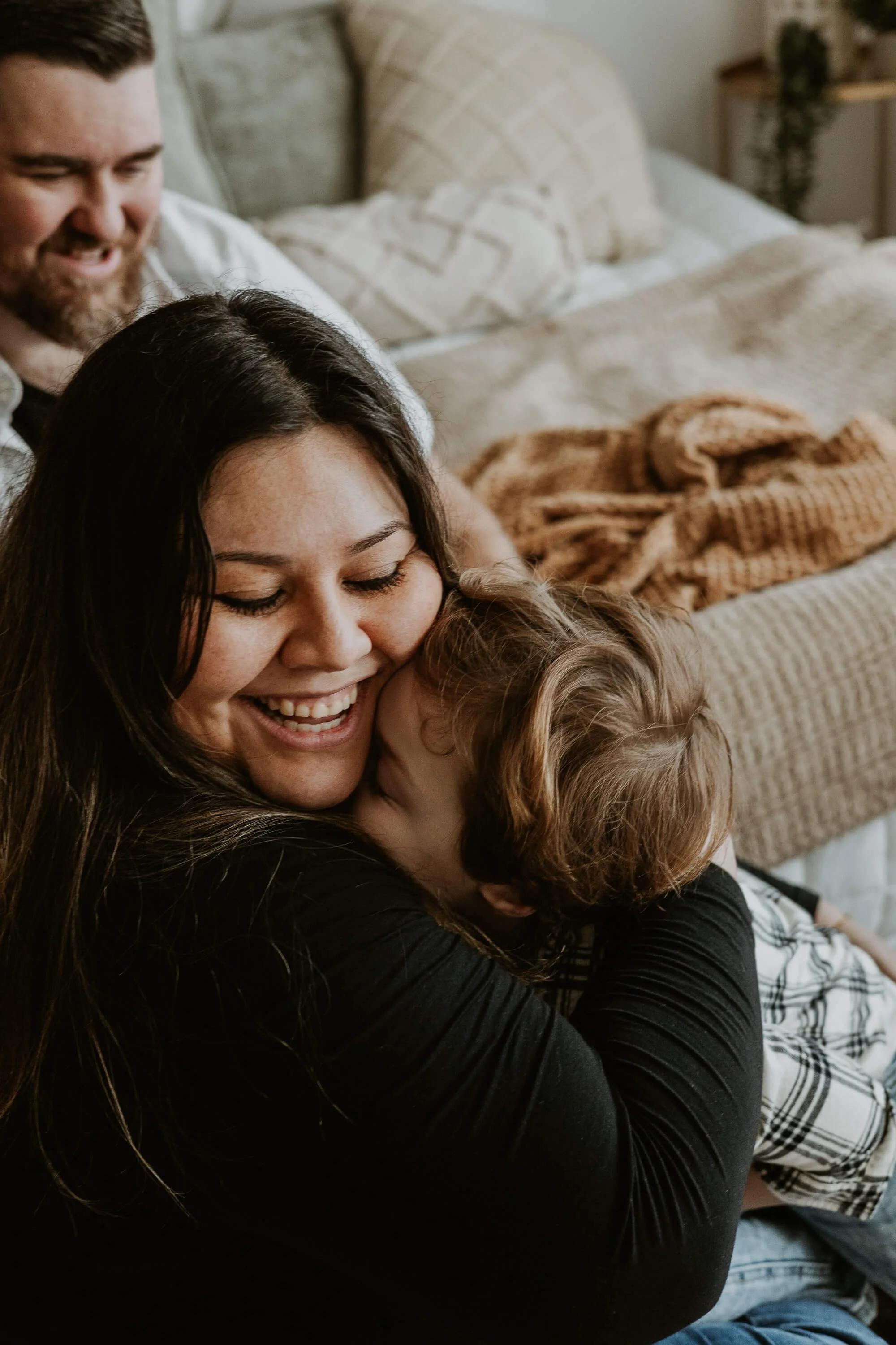 A mother smiles with laughter as her son squishes his face into her neck