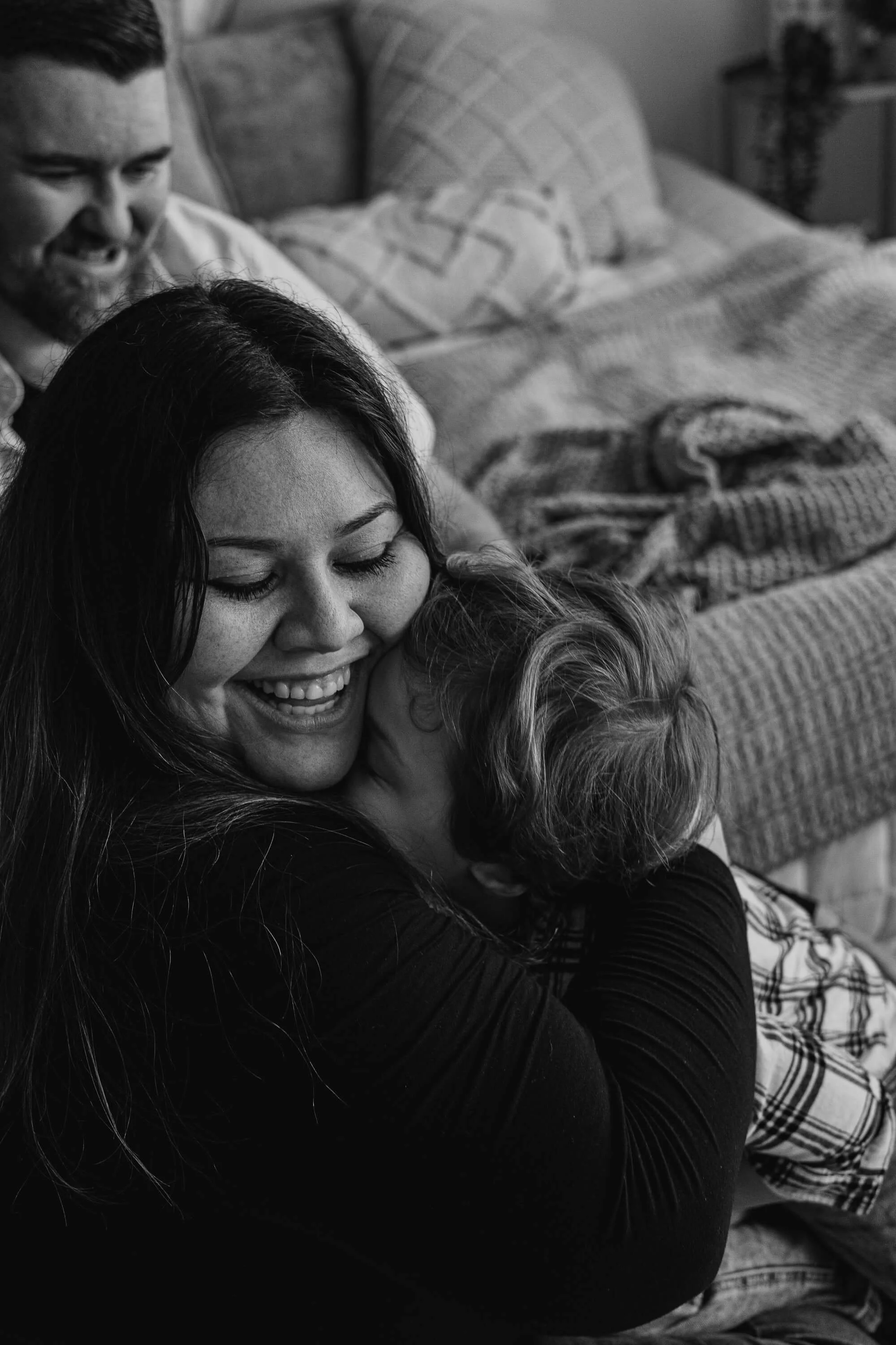 A mother laughs as her son squishes his face into her neck