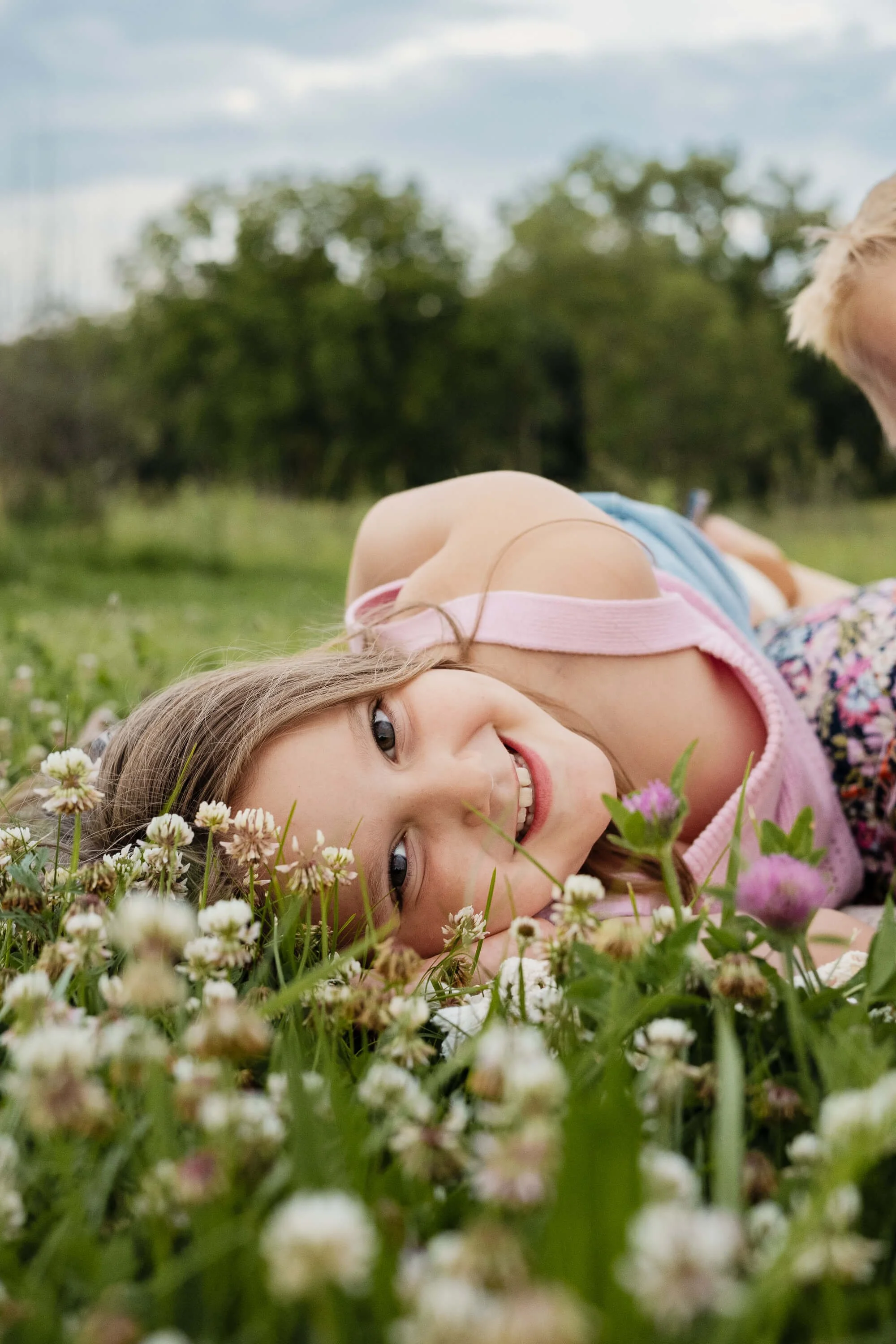 A seven year old girl lays in a field of clover smiling at the camera