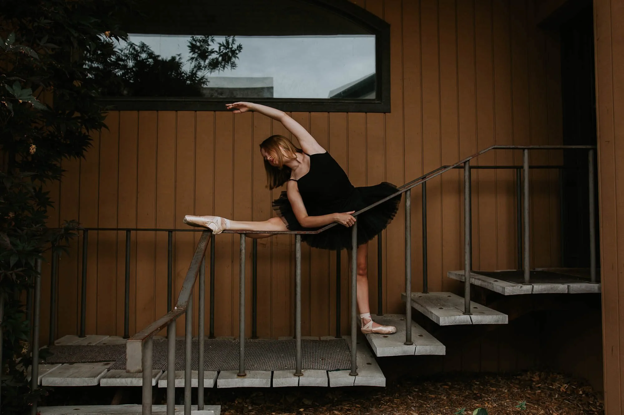 A dancer stretches on a staircase while her leg sits atop a railing.