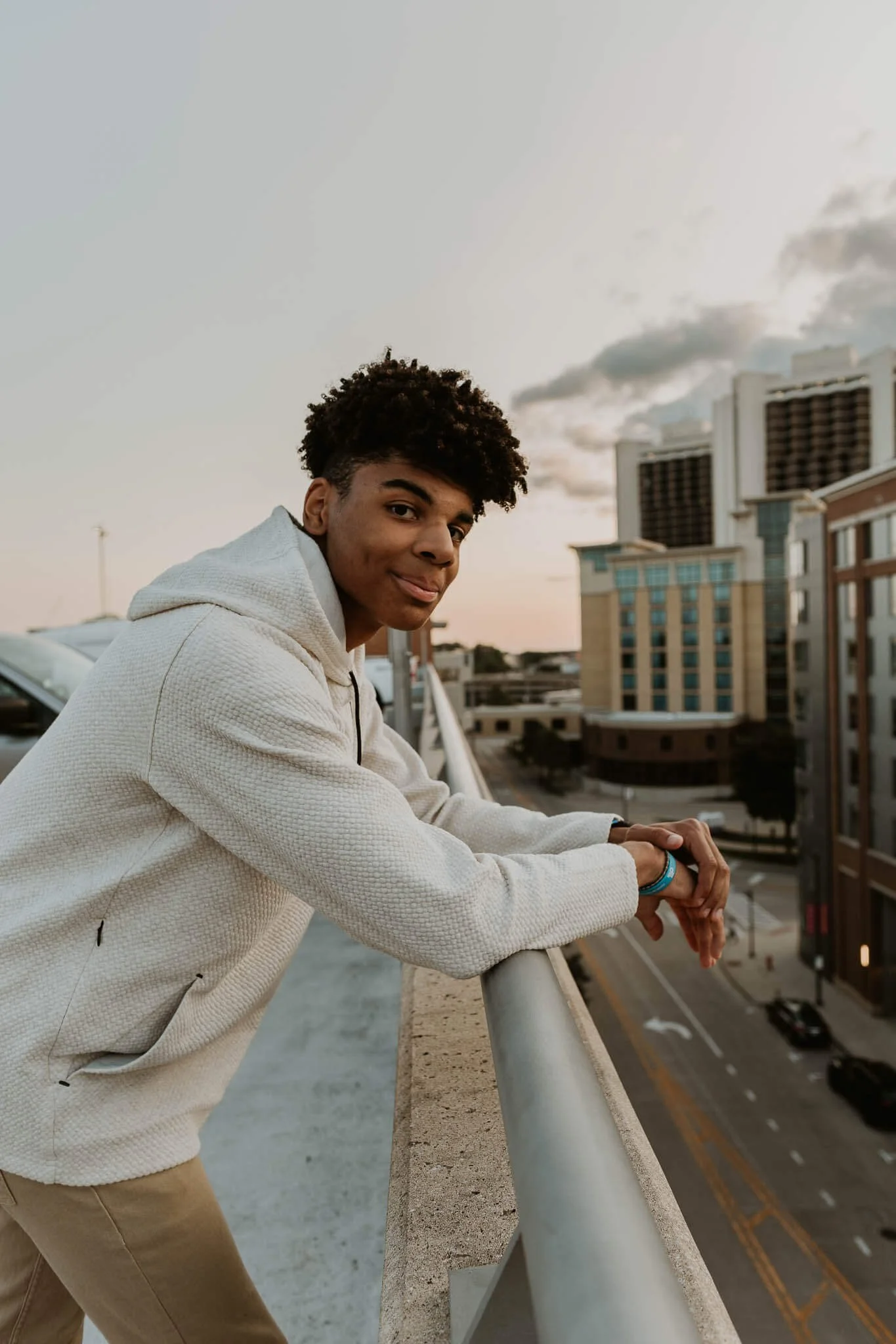 Leaning on the rail of a parking deck, a high school senior boy smiles.