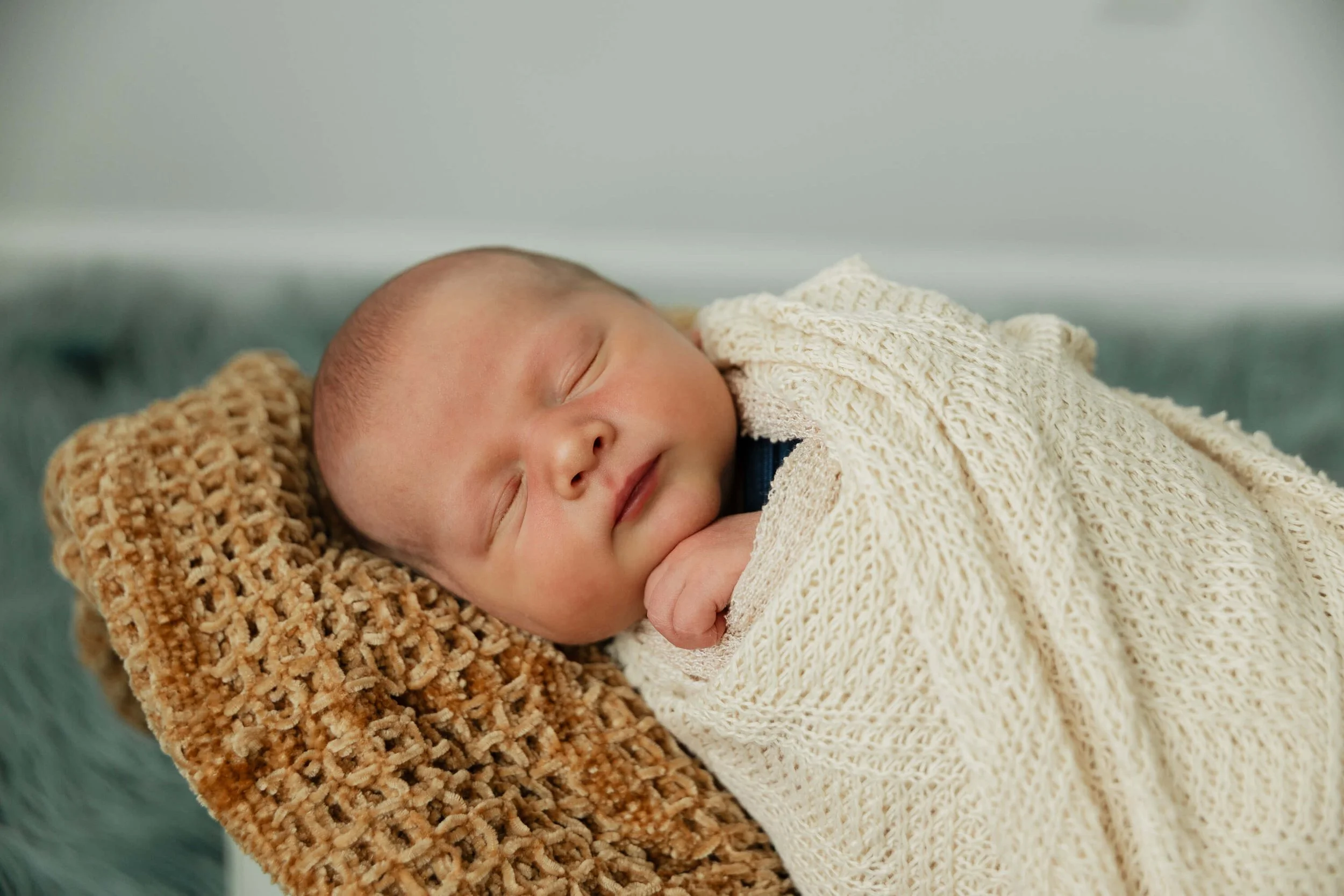 Sleeping peacefully, a baby boy is swaddled in a cream knit blanket