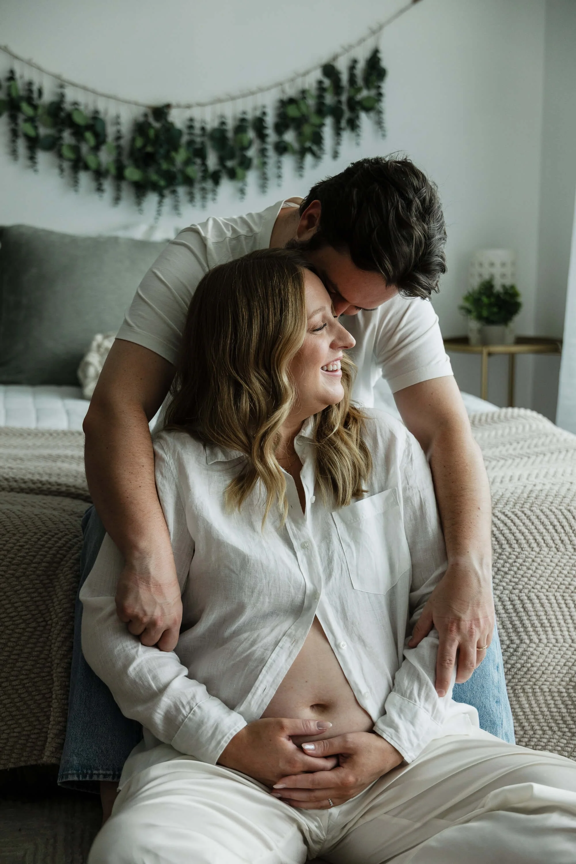 A couple snuggles in to one another on a bed while holding the woman's pregnant belly