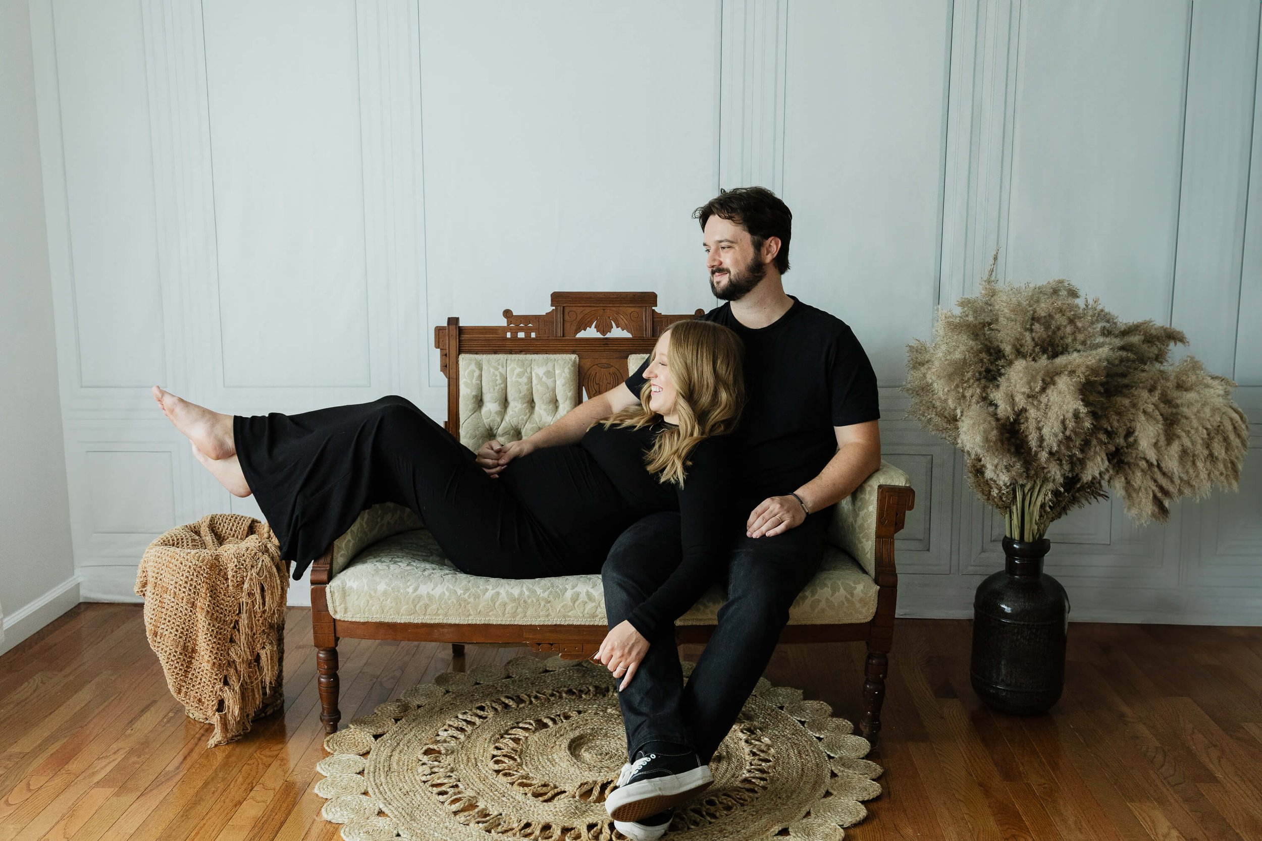 A pregnant woman lays in the lap of her husband on a couch as they snuggle